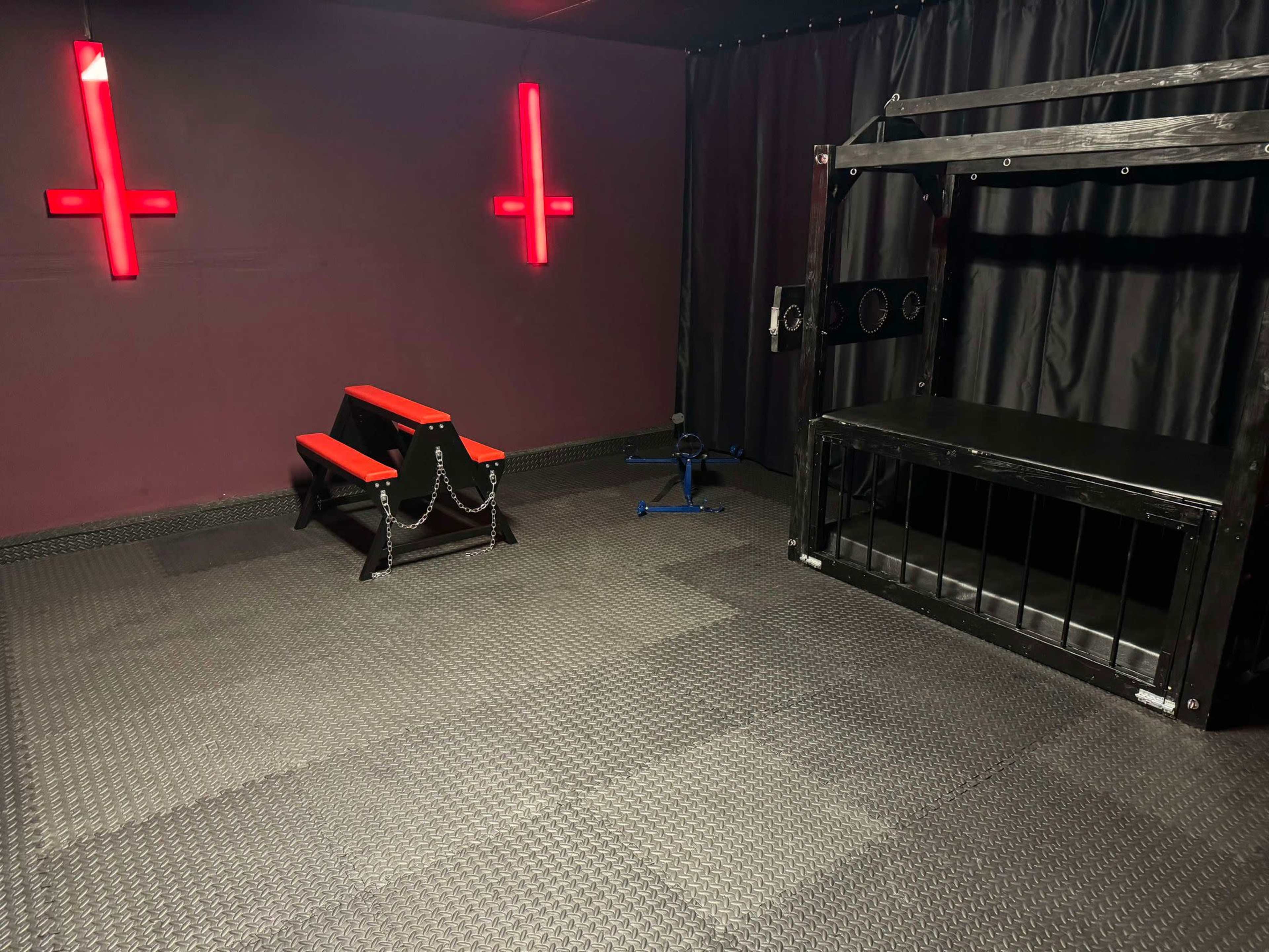The image shows a dimly lit room with red cross-shaped lights on the walls and gym equipment, including a bench and a cage-like structure.