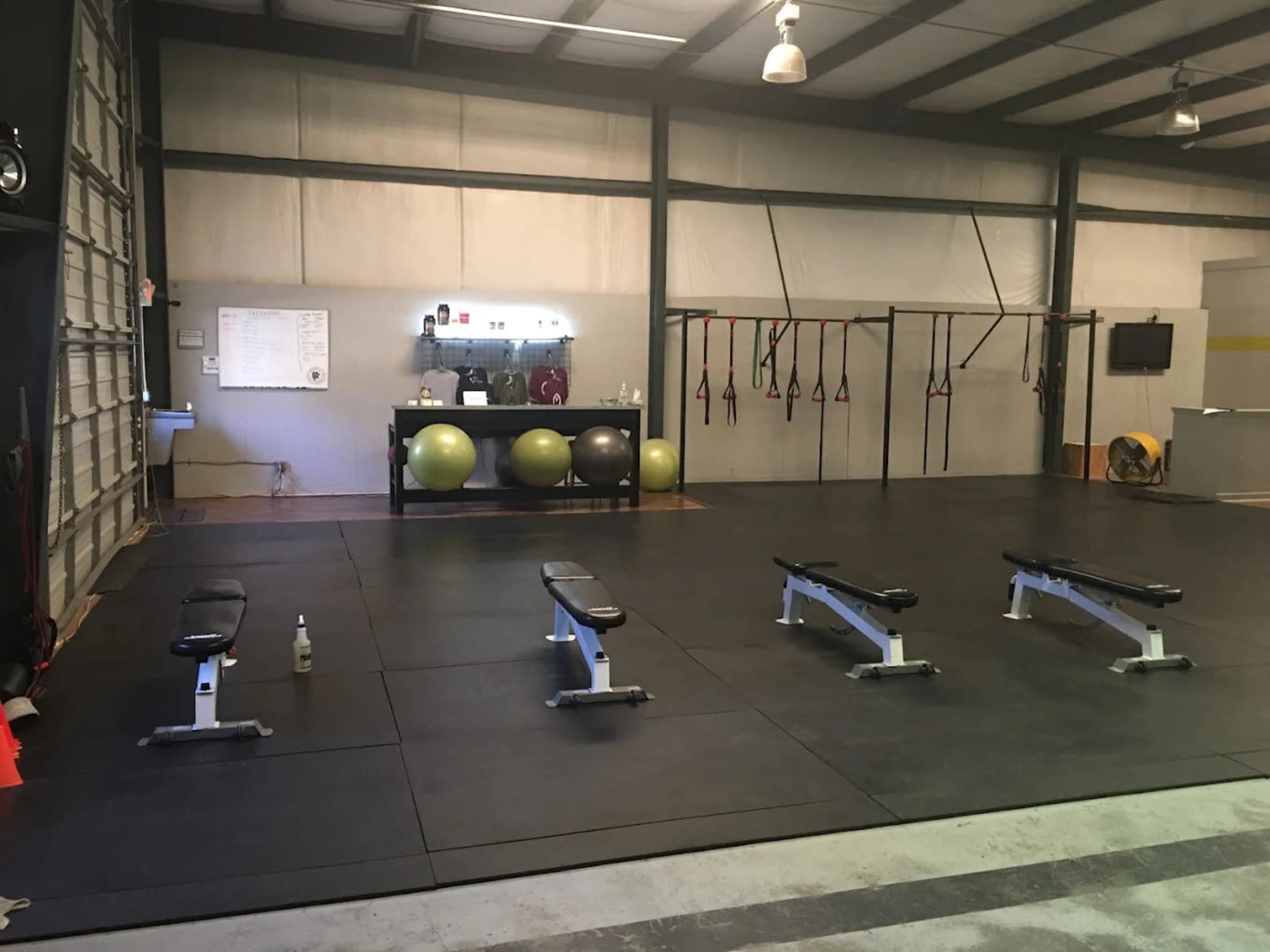 The image shows a spacious gym with several benches, exercise balls, and suspension training equipment arranged on a rubberized floor.