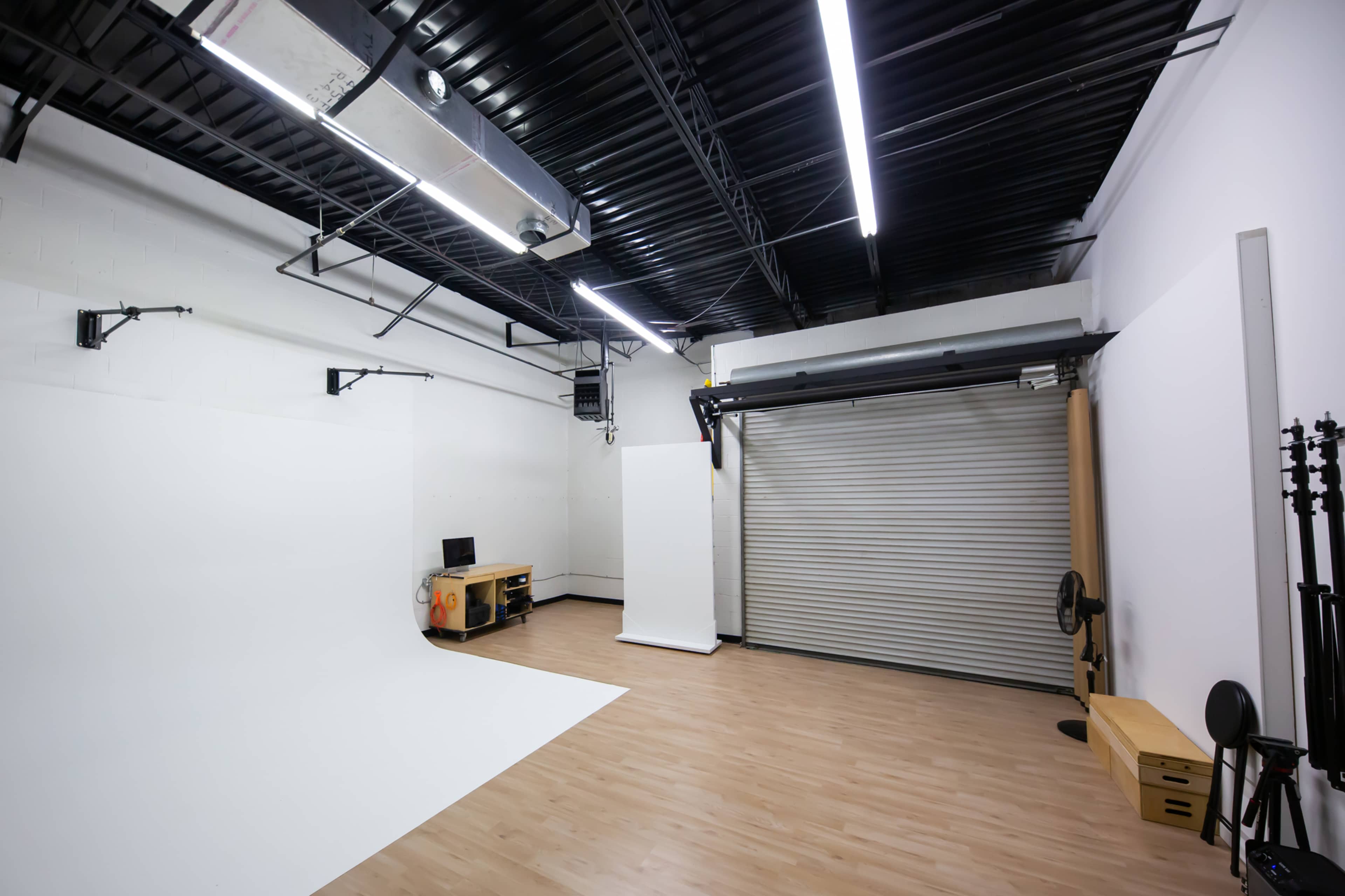 A spacious photography studio with a white backdrop, a computer setup, and equipment storage areas.