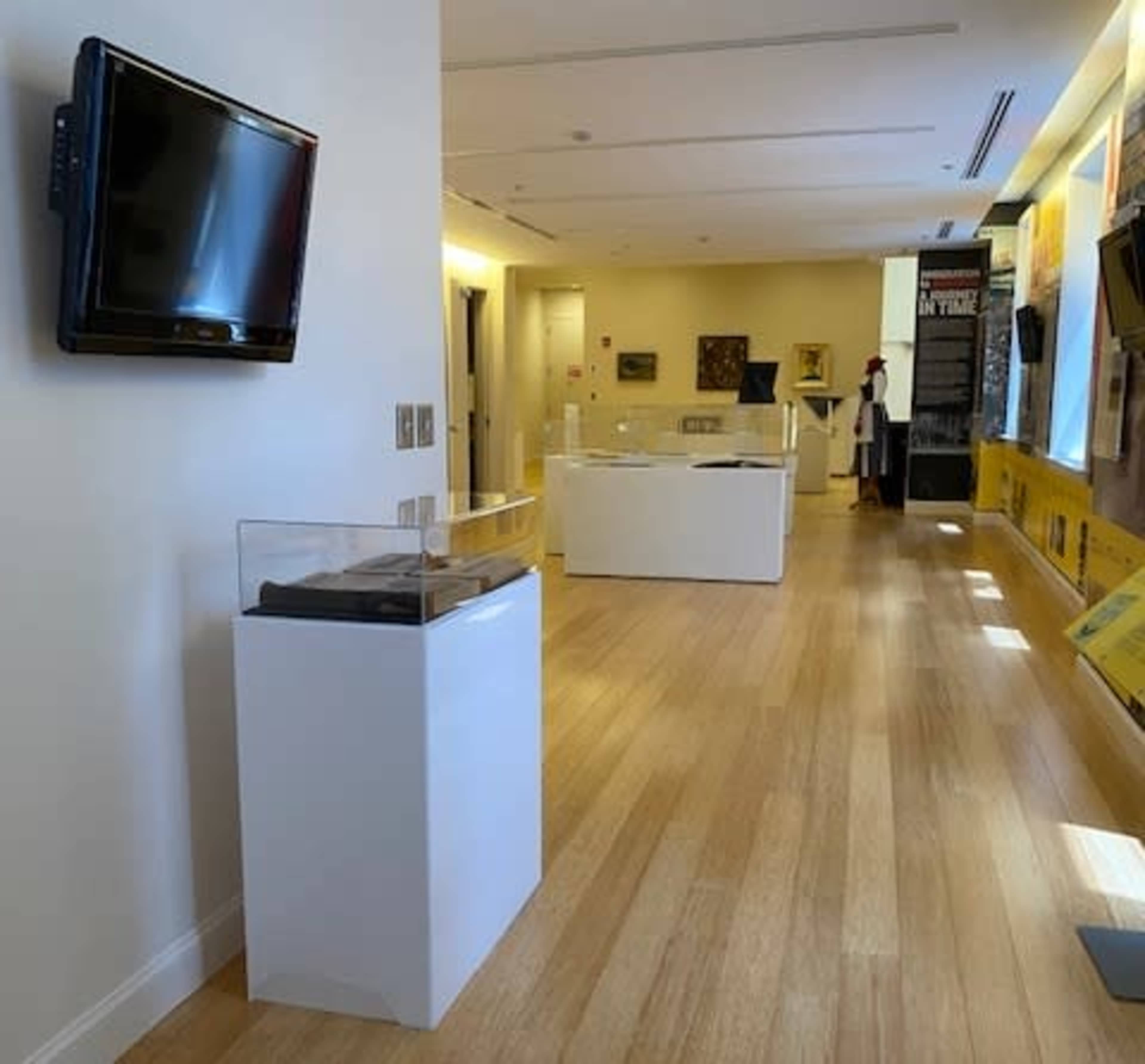 A modern exhibition space with wooden flooring, display cases, and a wall-mounted television.