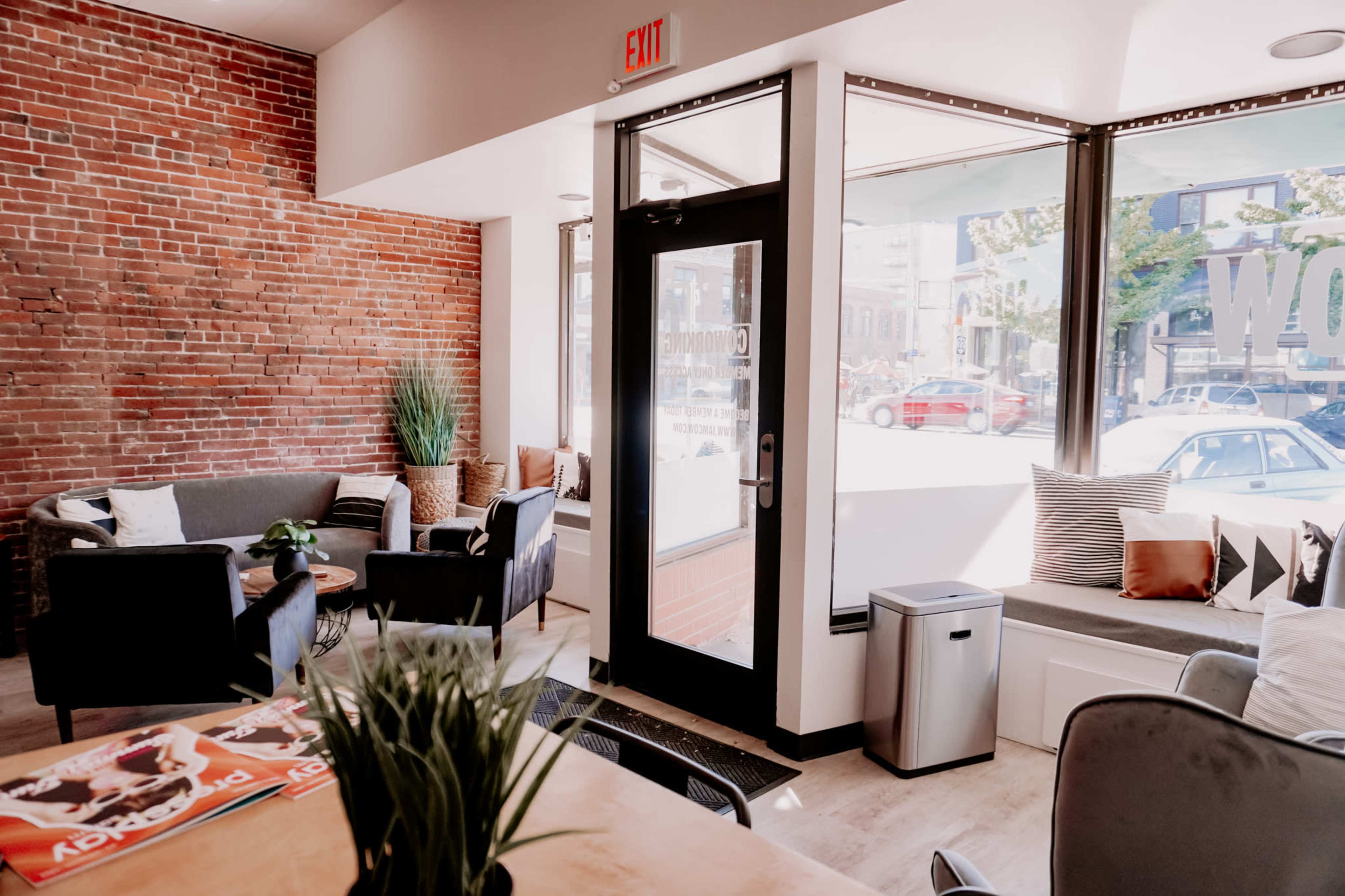 A cozy café interior with exposed brick walls, seating areas featuring sofas and chairs, and large windows allowing natural light in.