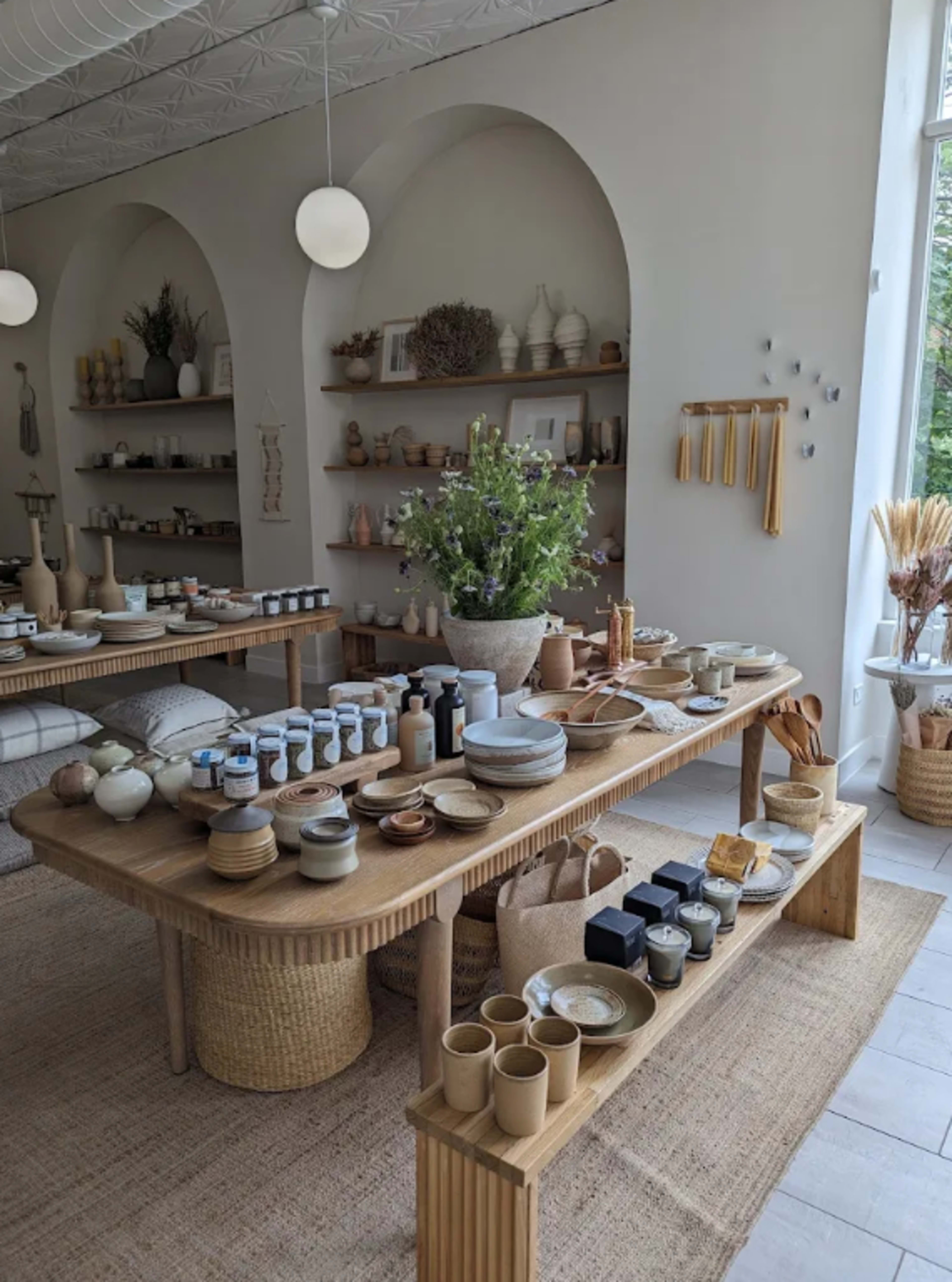 The image shows a boutique interior filled with various ceramic and pottery items displayed on wooden tables and shelves.
