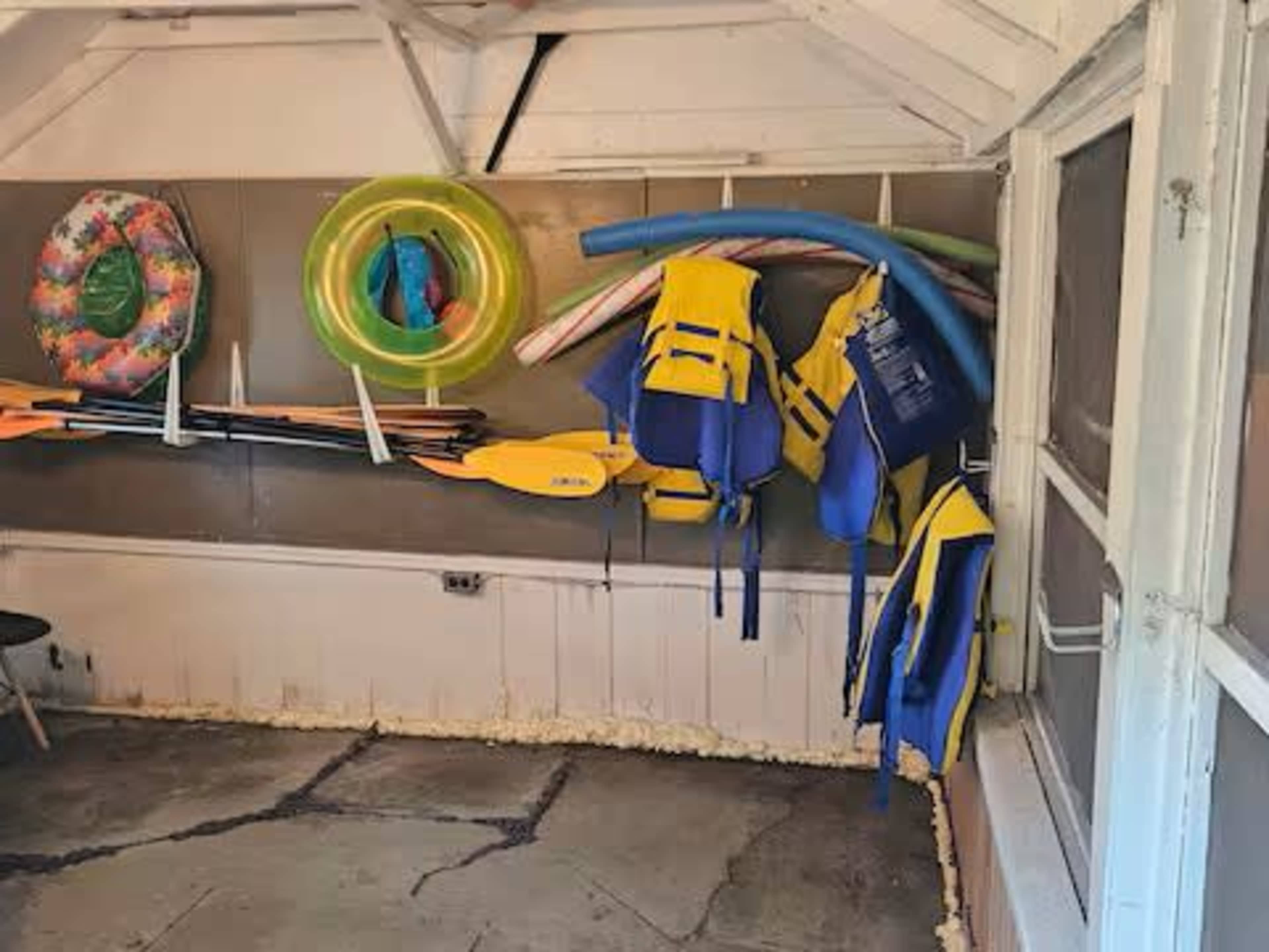 The image shows a storage area with life vests, paddles, and inflatable rings hanging on the wall.