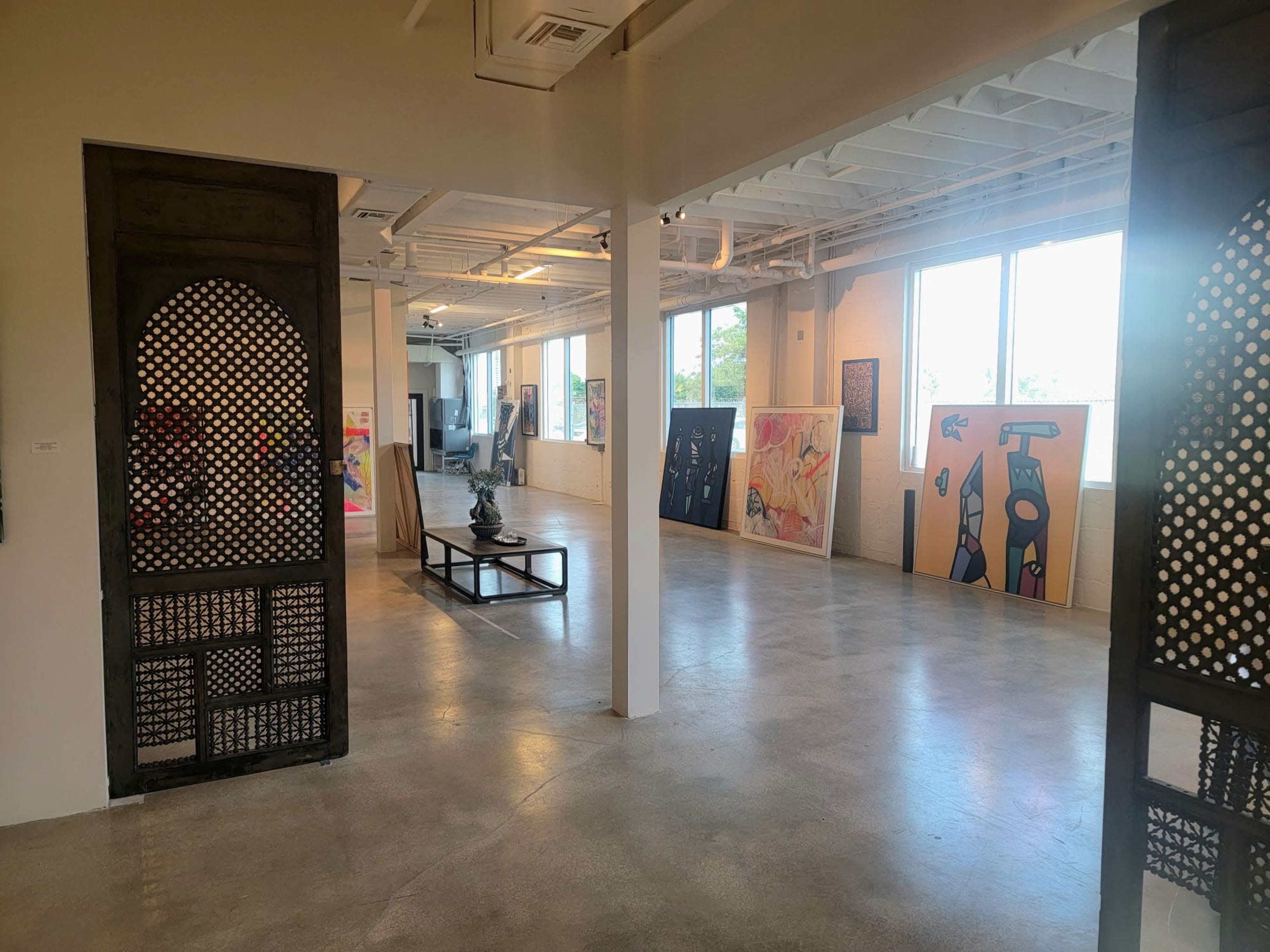An art gallery with a polished concrete floor, featuring several colorful artworks displayed along the walls and a sculpture in the center.