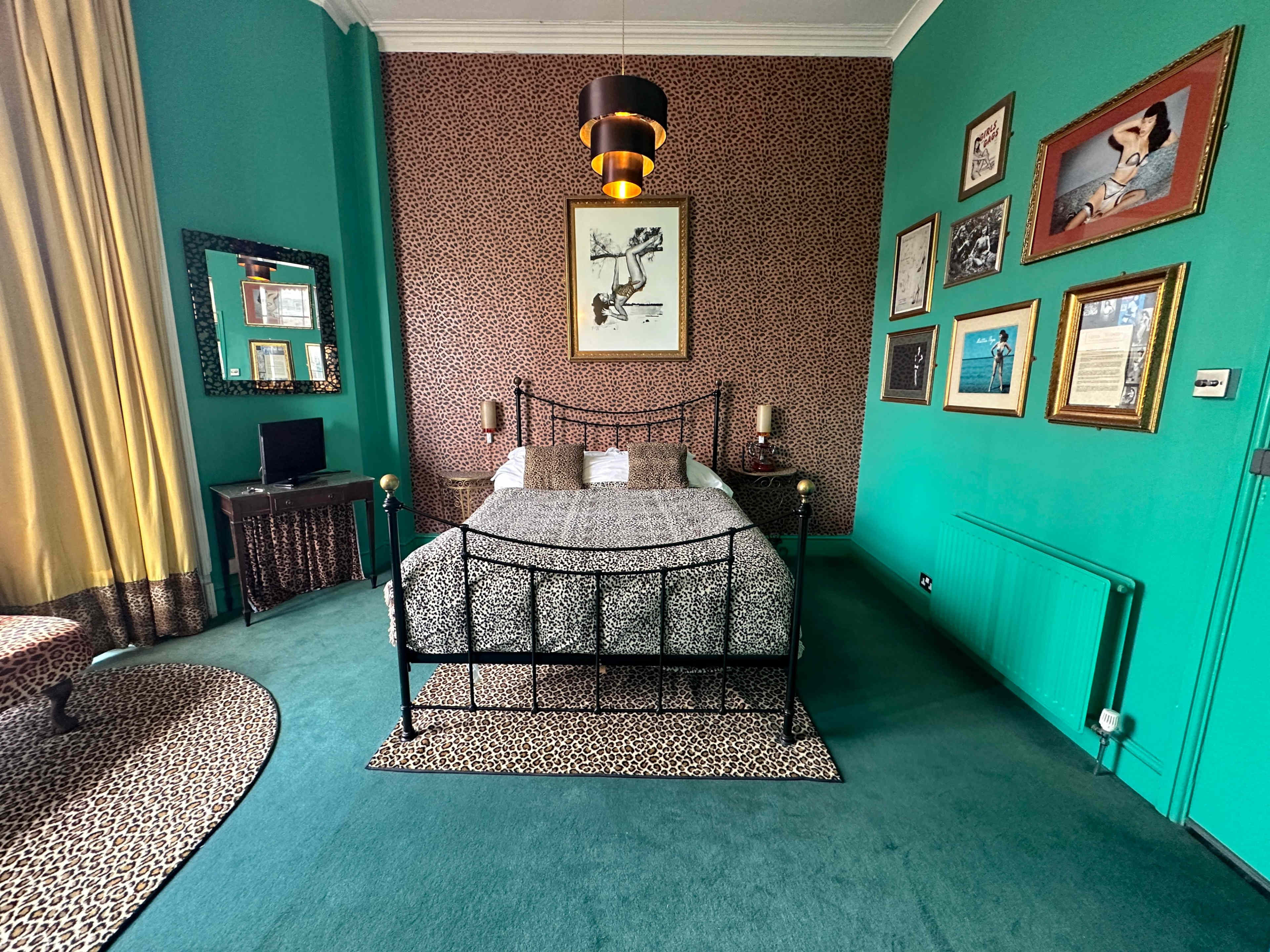 A vibrant bedroom featuring a bed with a patterned duvet, green walls, a leopard-print rug, and framed artwork on the walls.