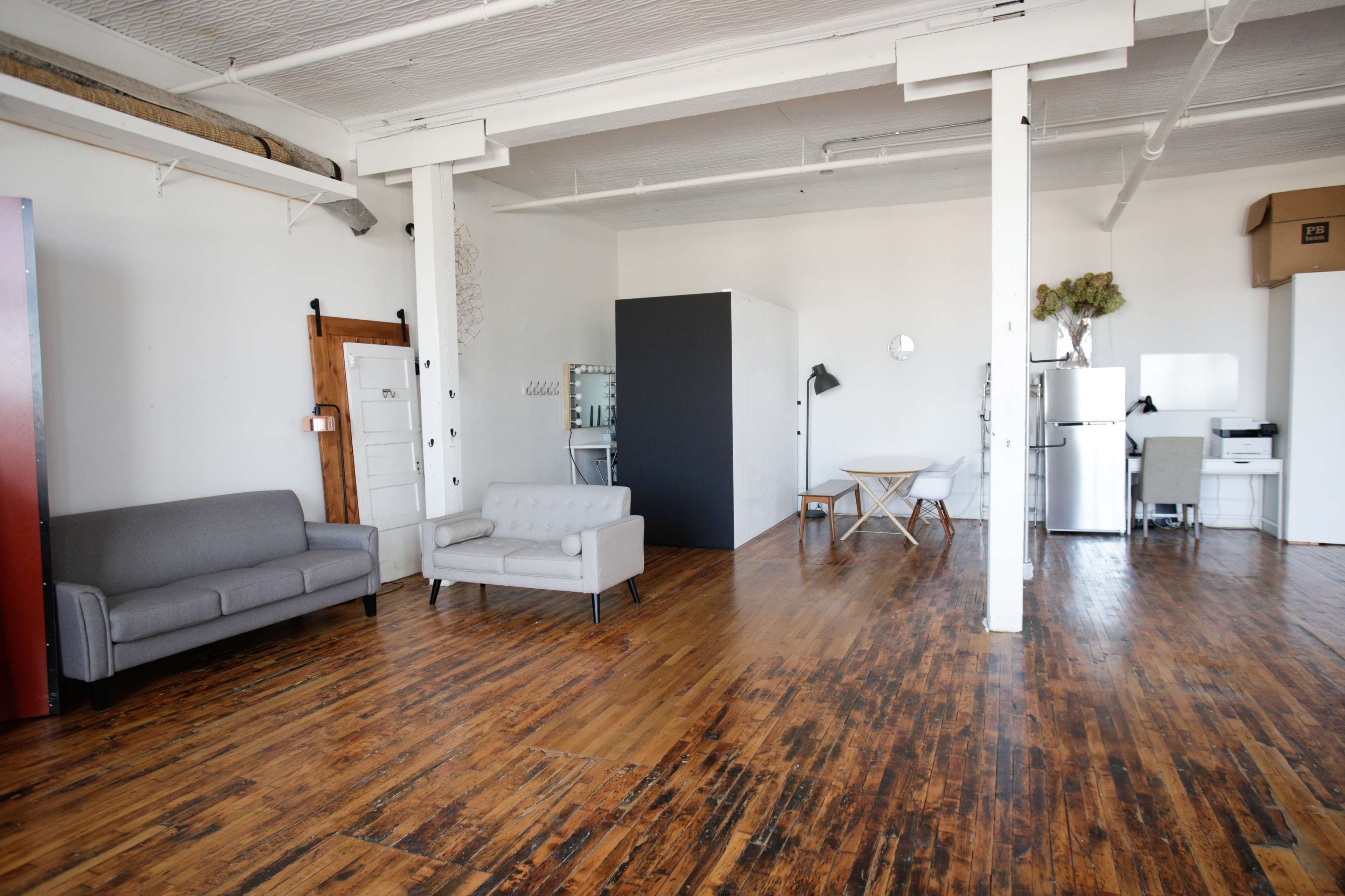A spacious, minimalist room with wooden flooring, featuring a gray sofa, a small table, and various pieces of furniture against white walls.