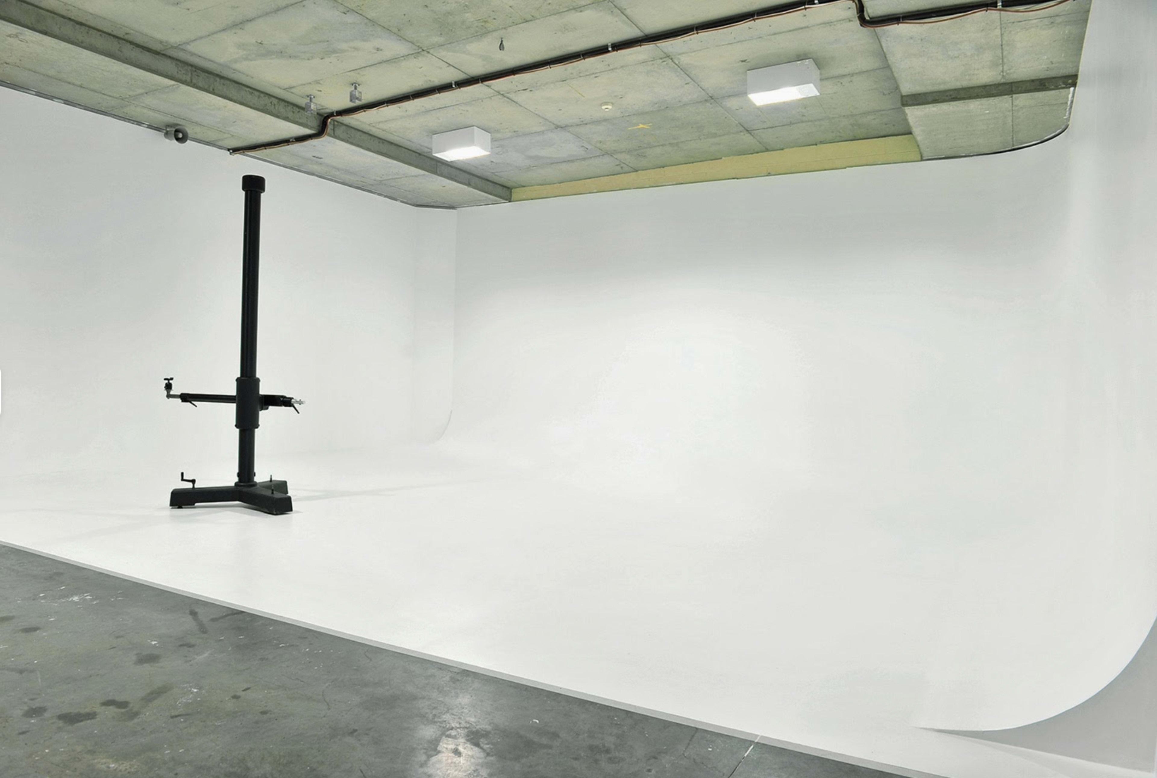 An empty studio space with a seamless white backdrop and a backdrop support stand in the center.