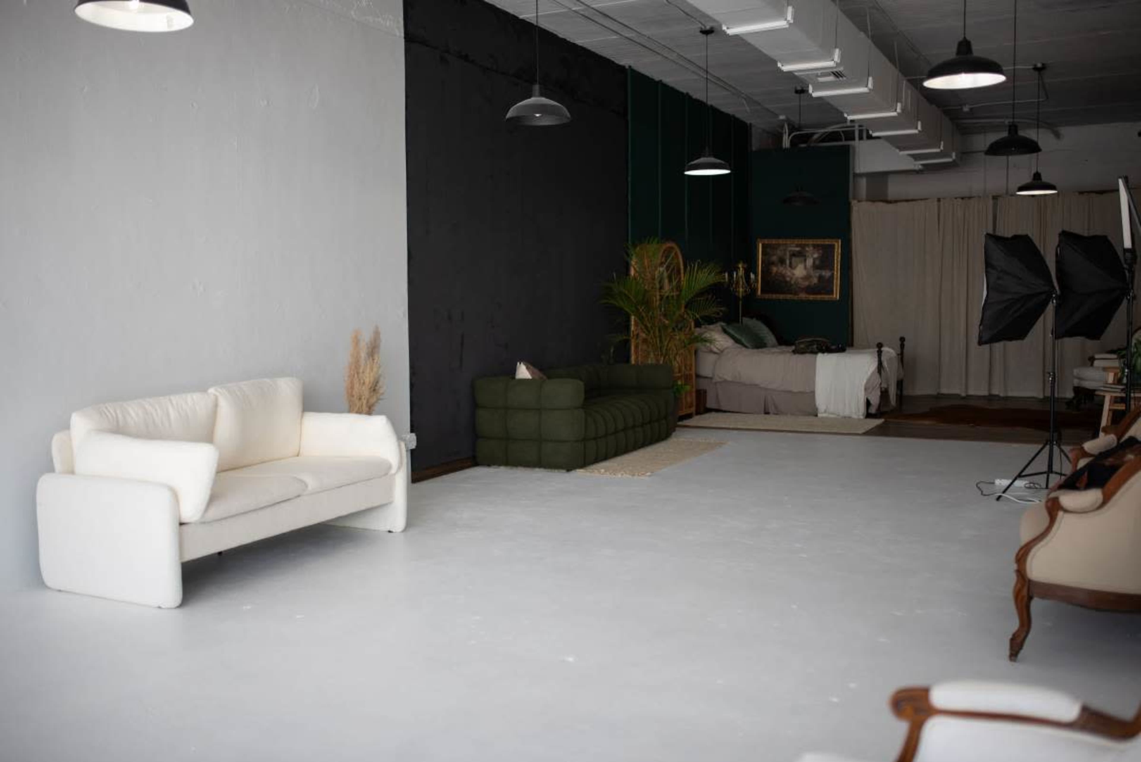 A spacious, minimalist room with two sofas, a bed in the background, and lighting equipment set up for a photo shoot.