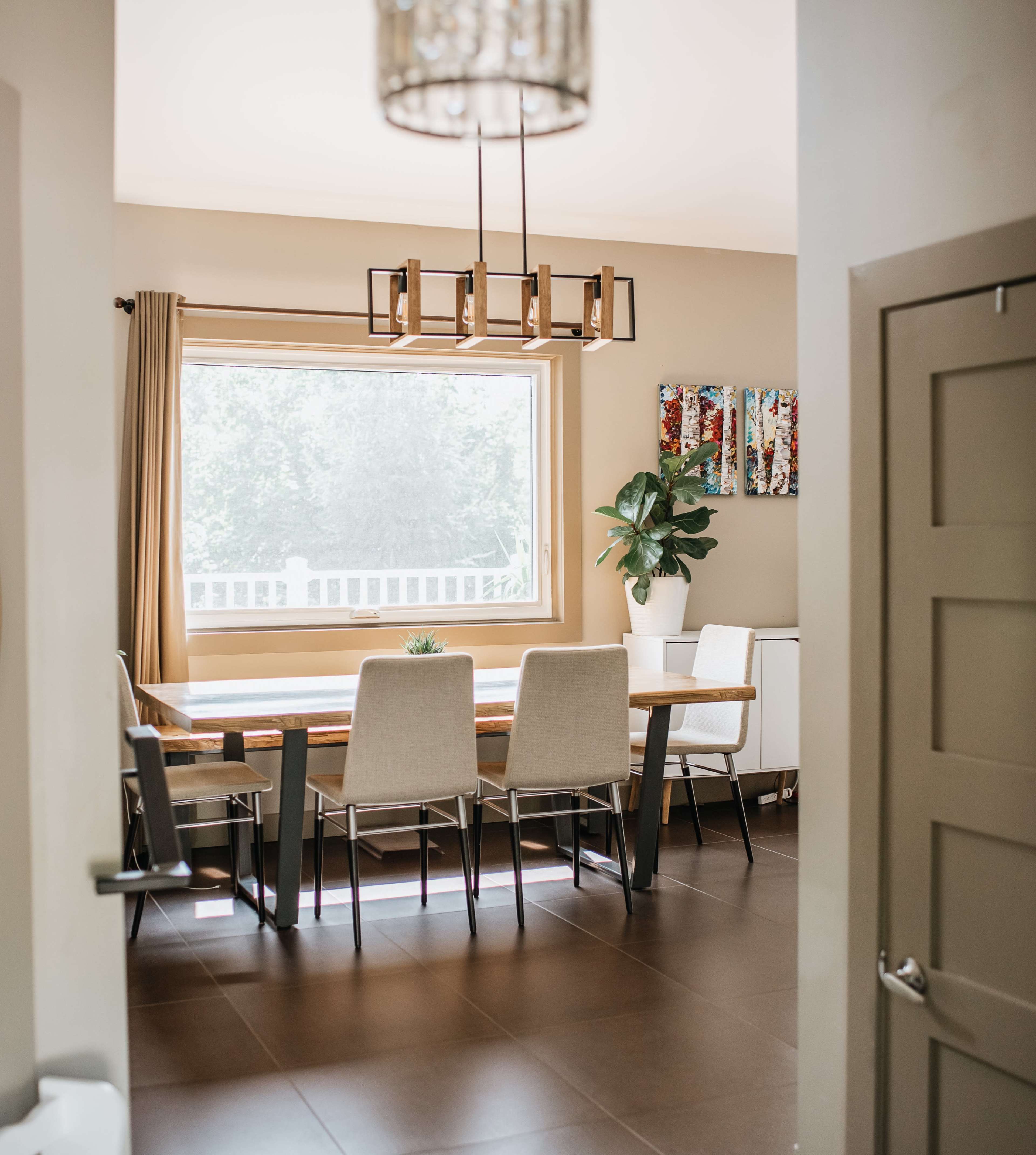 A dining room features a wooden table surrounded by upholstered chairs, with a large window providing natural light.