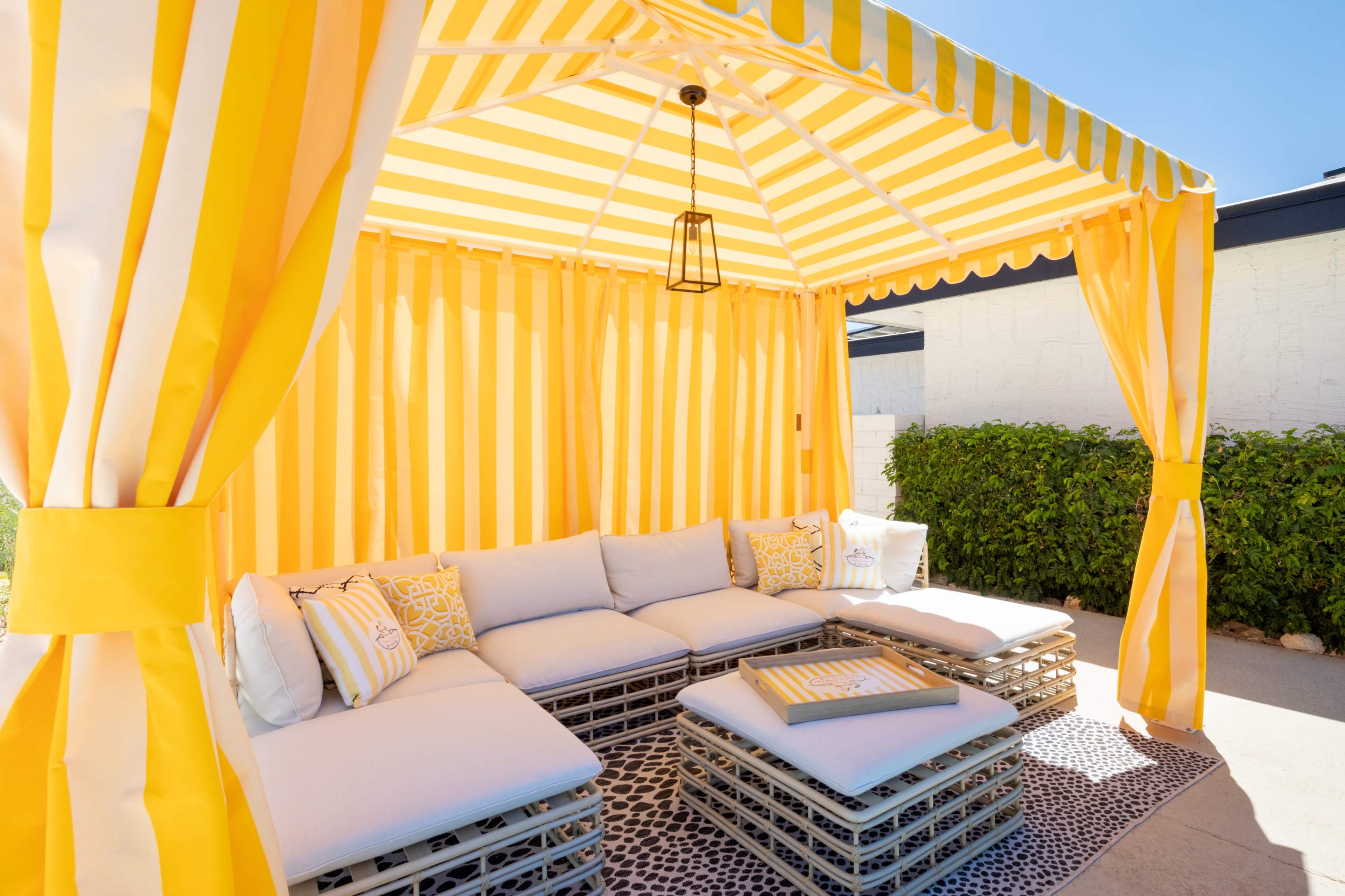 A yellow and white striped outdoor cabana with a cushioned seating area and a small coffee table.