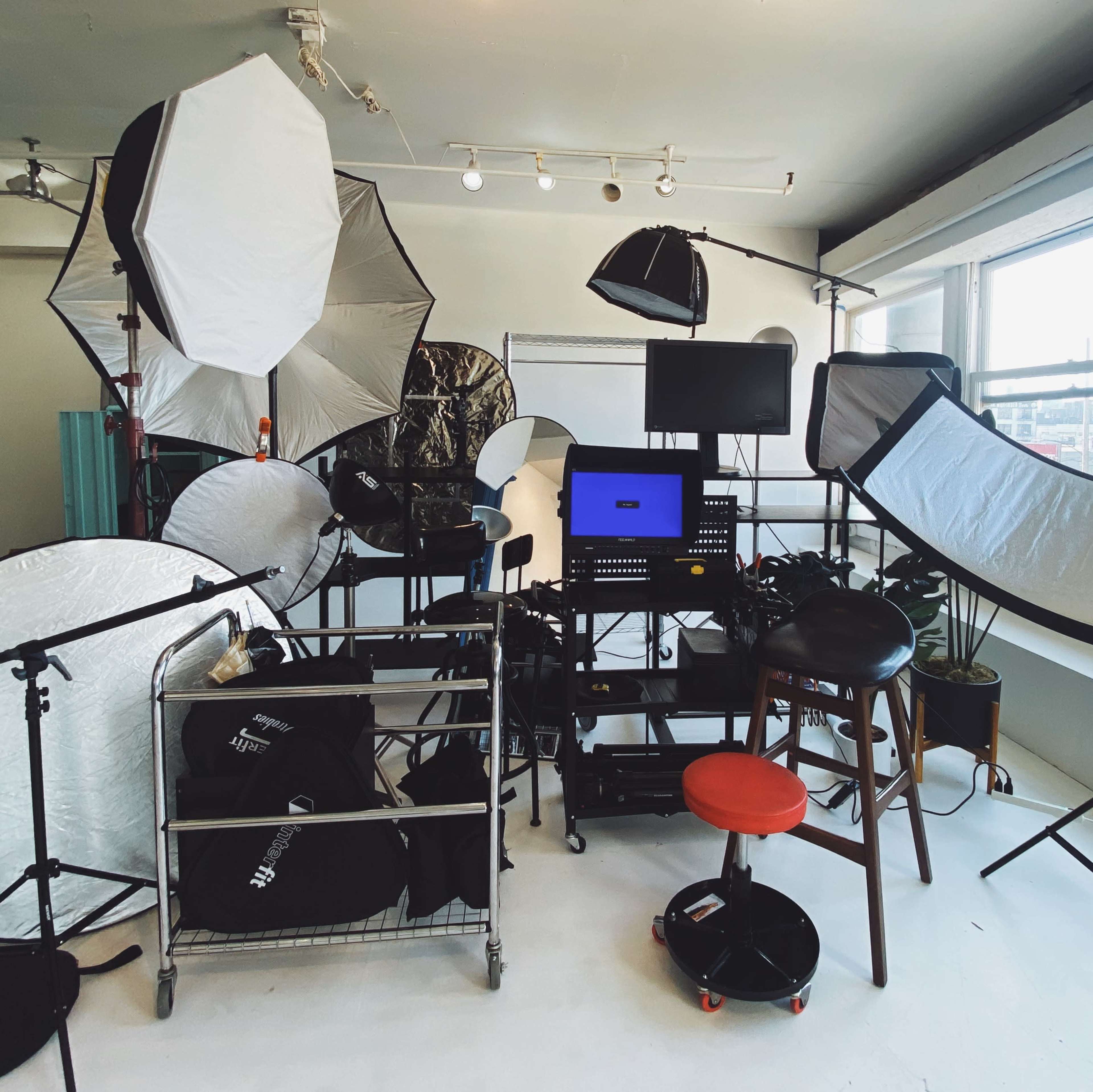 The image shows a photography studio filled with various lighting equipment, backdrops, and a workstation organized on a cart.