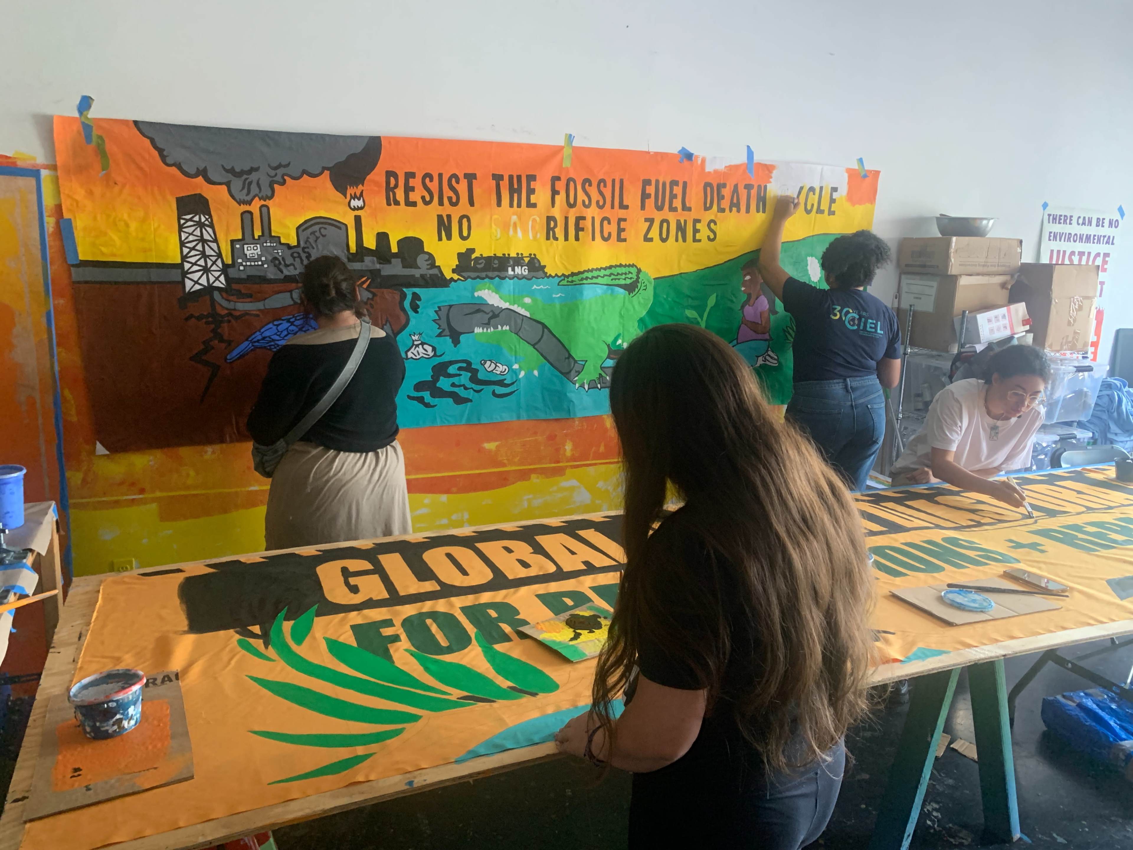 A group of people is painting large, colorful banners with environmental messages on a wall in a community space.