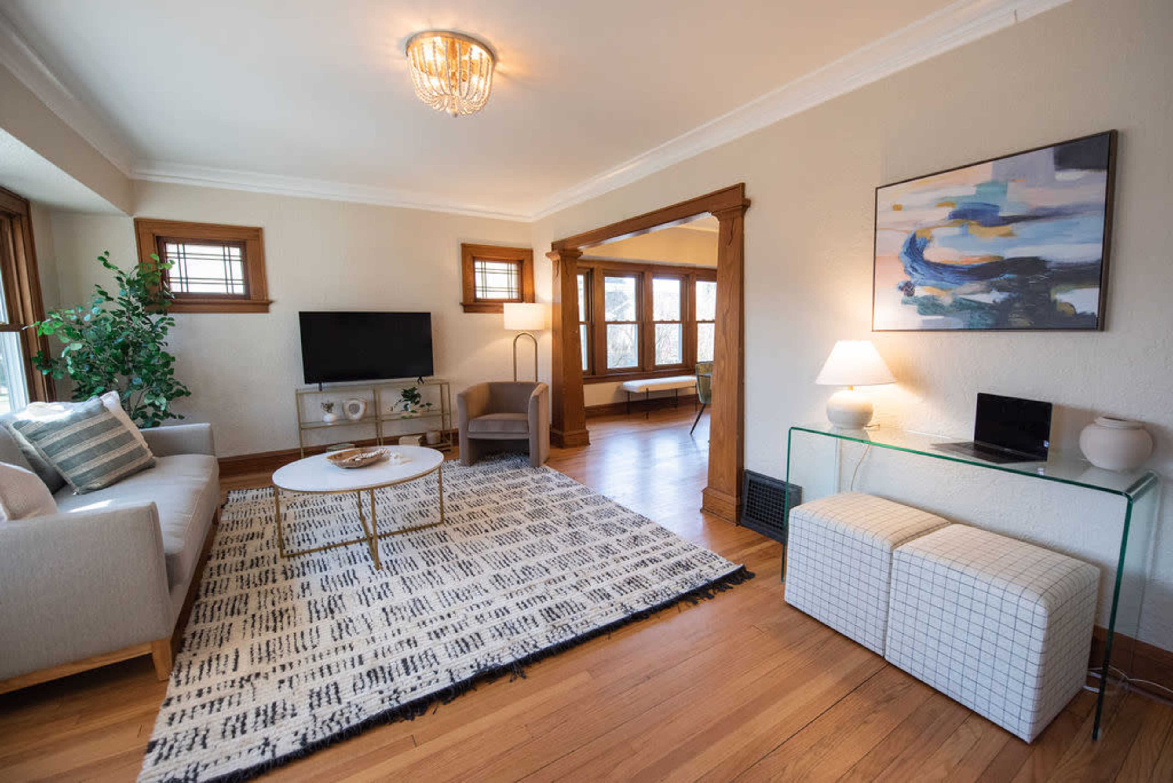 The living room features a light sofa, a mounted television, a coffee table on a patterned rug, and a glass side table beside a lamp.