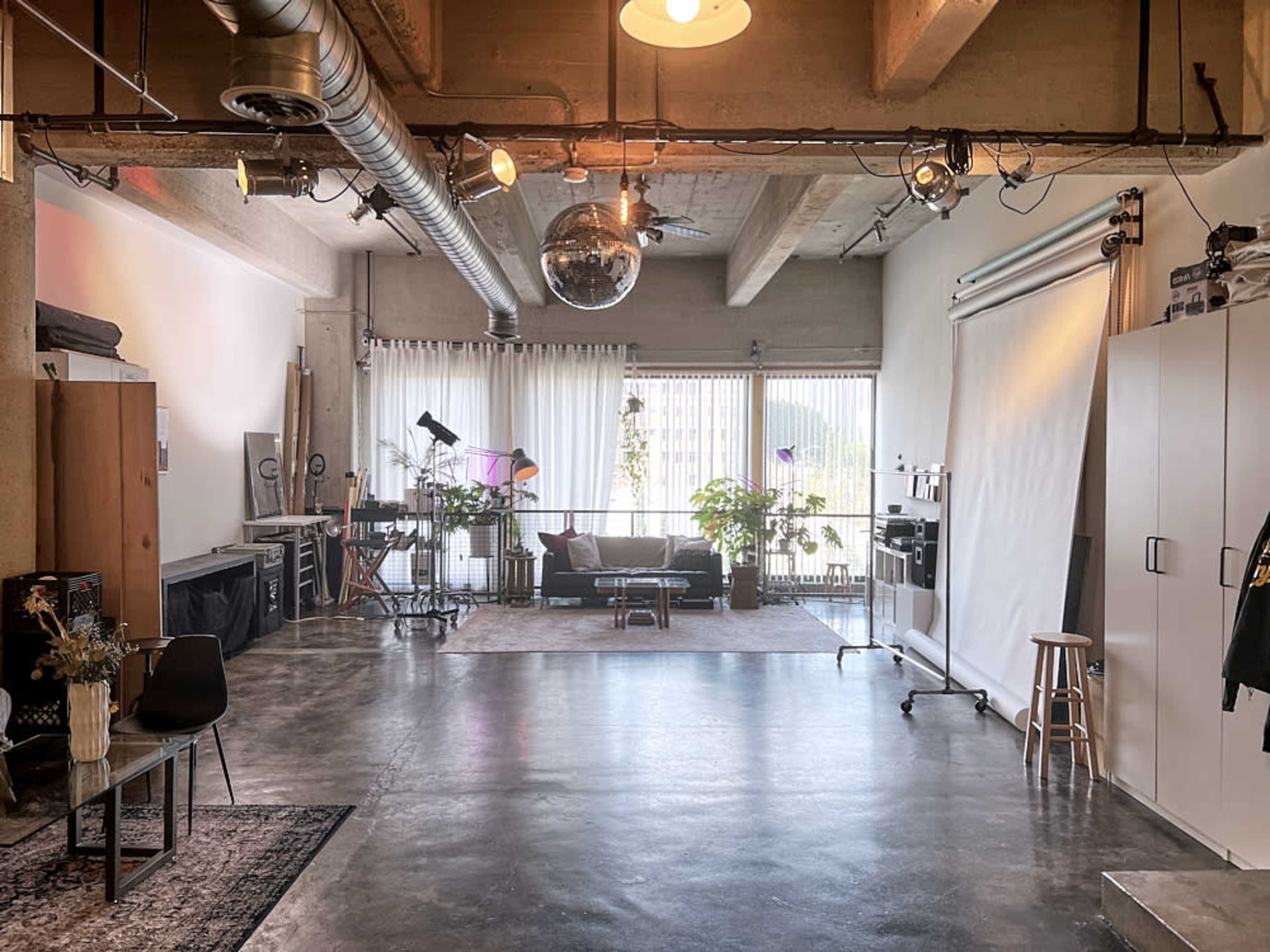 The scene depicts a modern studio space with large windows, a seating area, and photography equipment arranged around a central backdrop.