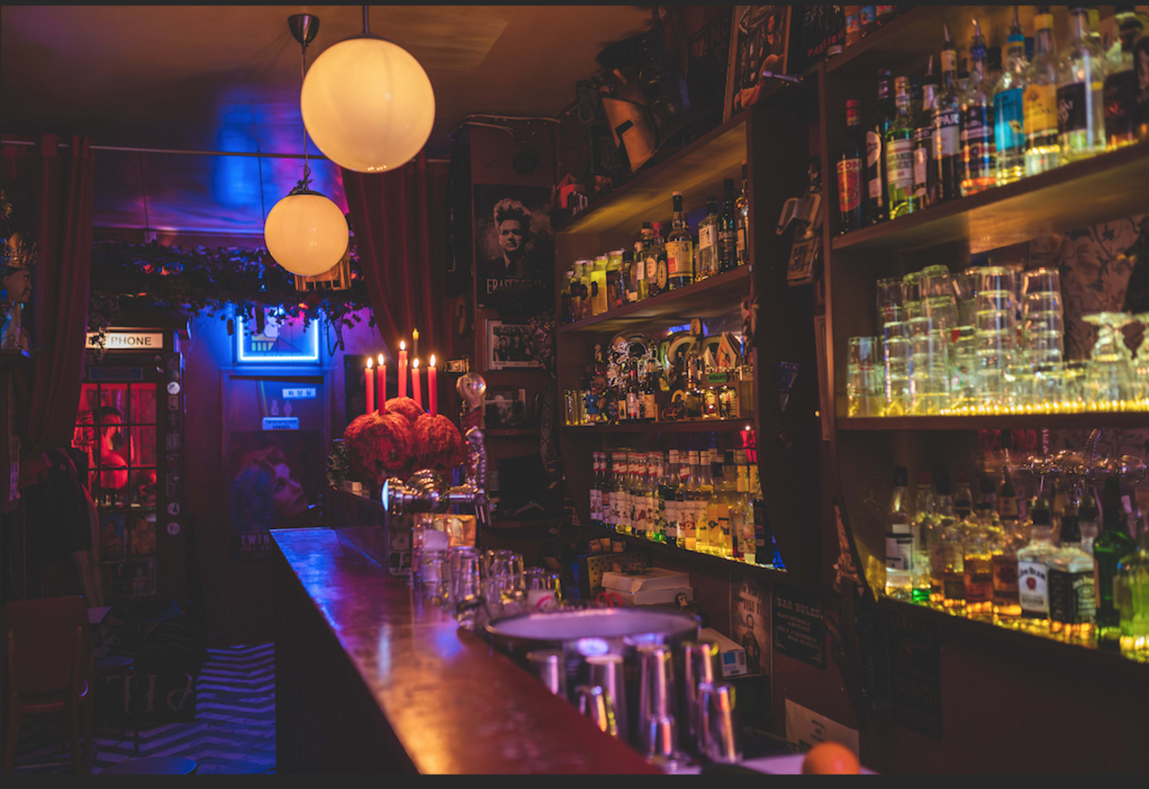 A dimly lit bar features shelves stocked with various bottles, illuminated by soft lighting and candlelight.