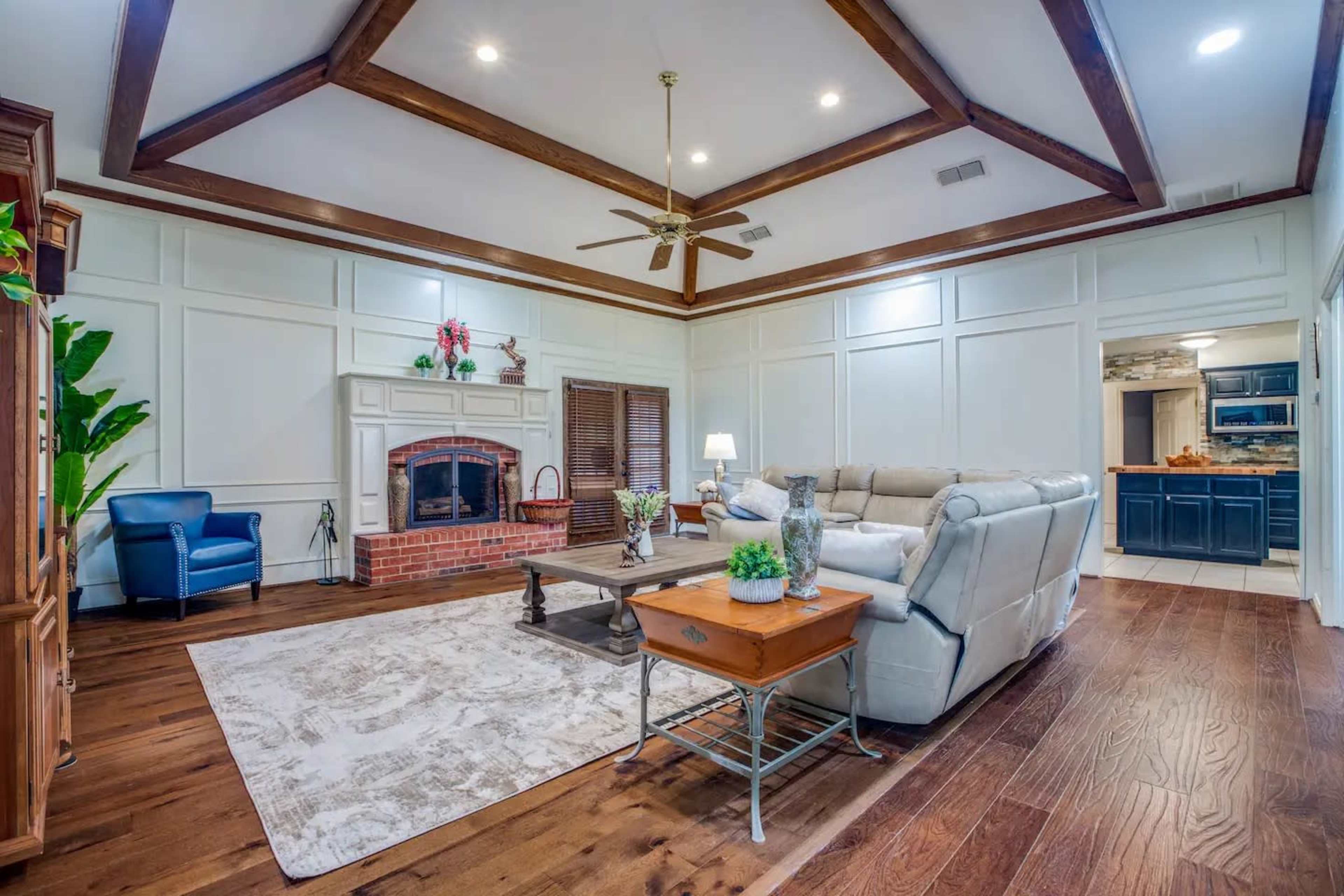 A living room with a coffered ceiling, a brick fireplace, and a mix of modern and traditional furniture arranged around a central coffee table.