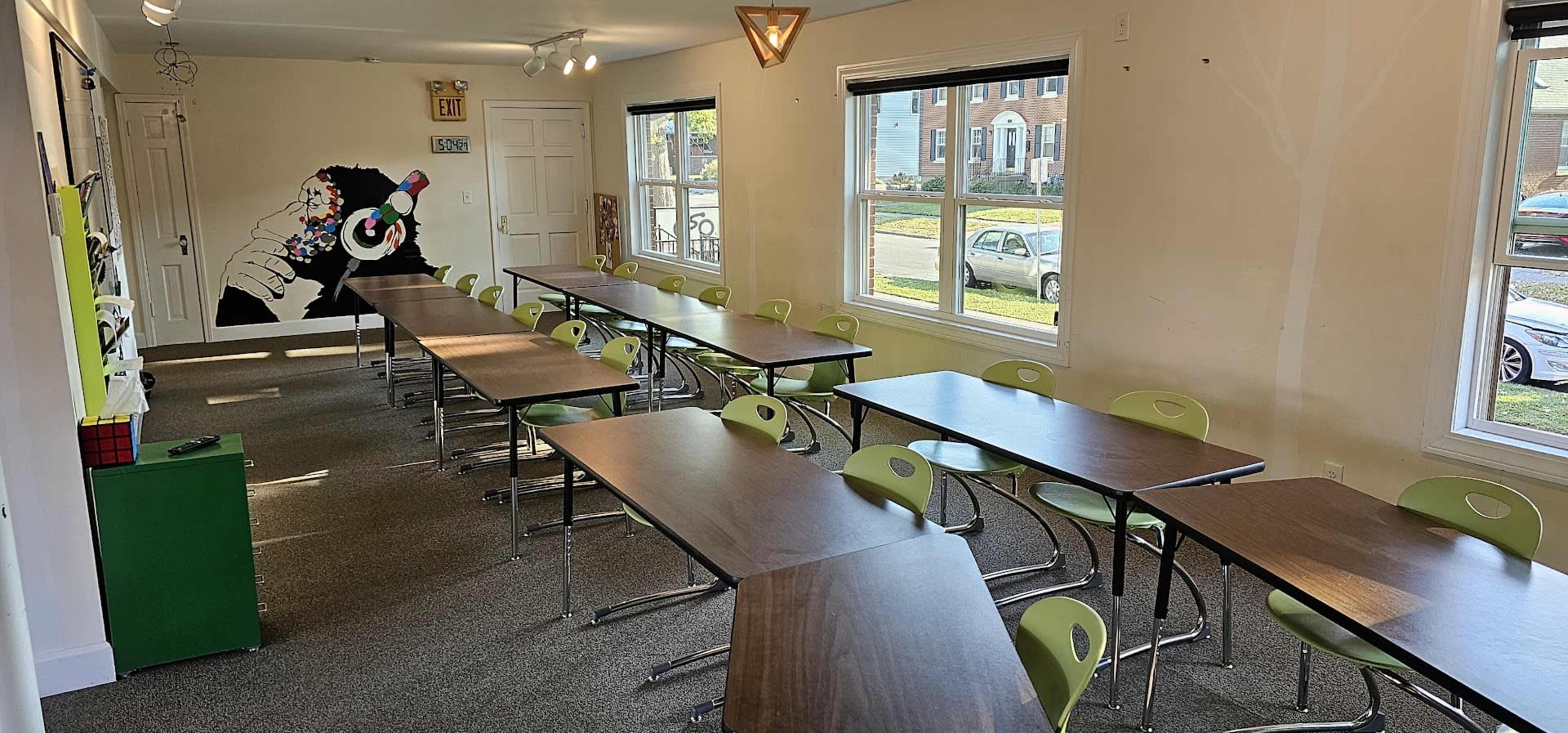 A classroom setup with several rows of tables and chairs, illuminated by natural light from windows.