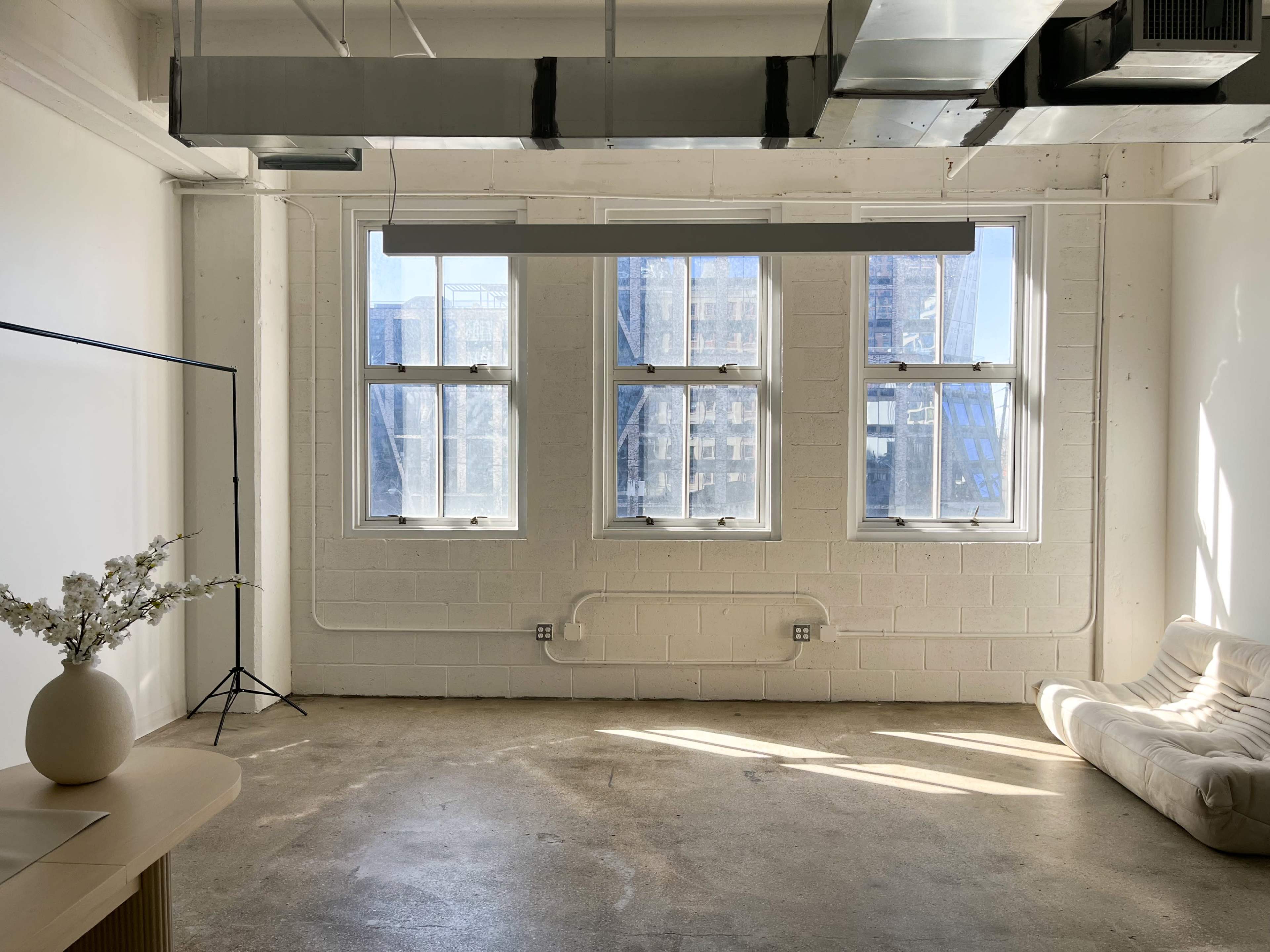 A minimalist room with large windows, a neutral-colored sofa, a light-colored table, and a simple decorative arrangement in front of the windows.