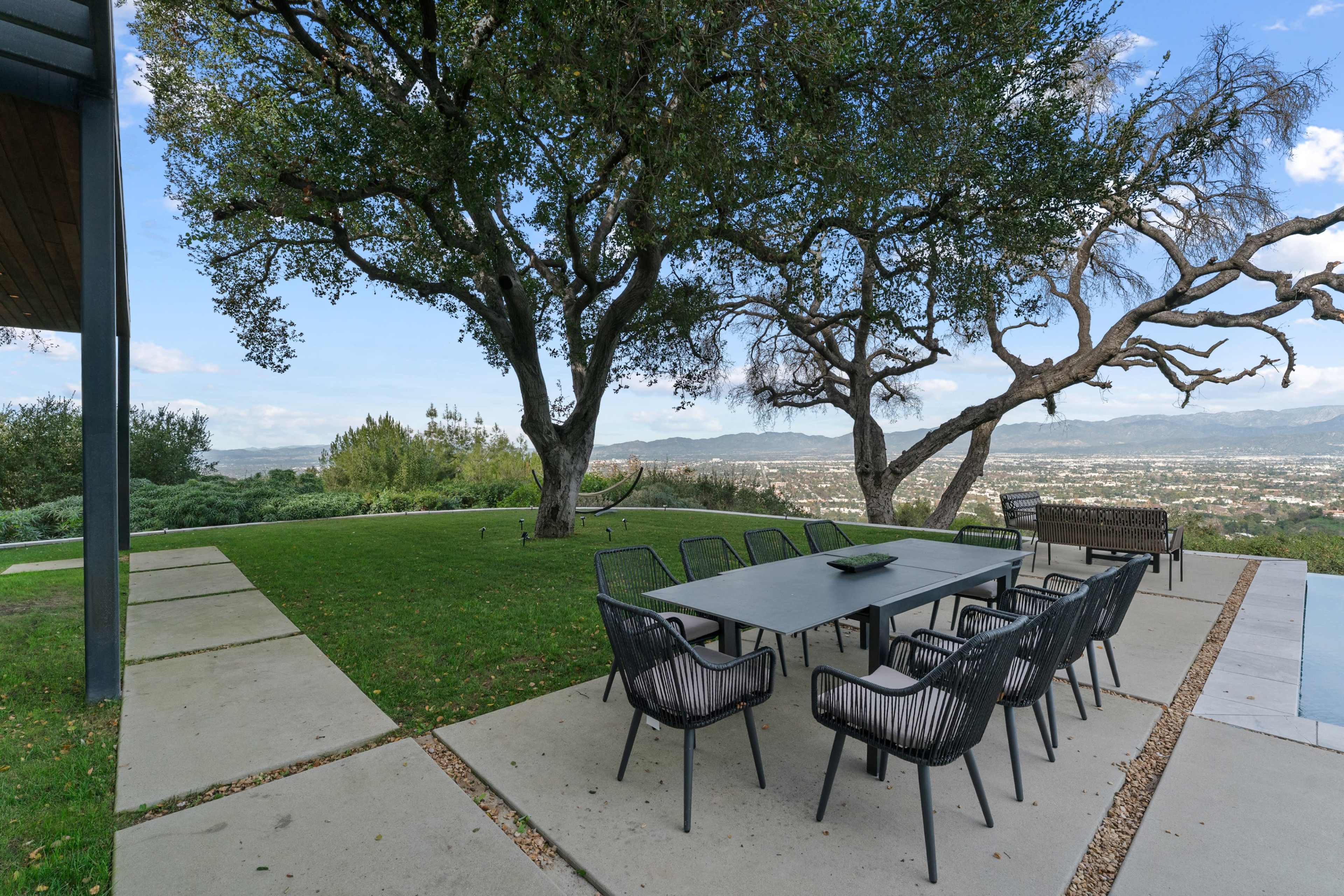 A modern outdoor dining area features a large table with chairs set on a patio overlooking a scenic view of the valley and distant mountains.
