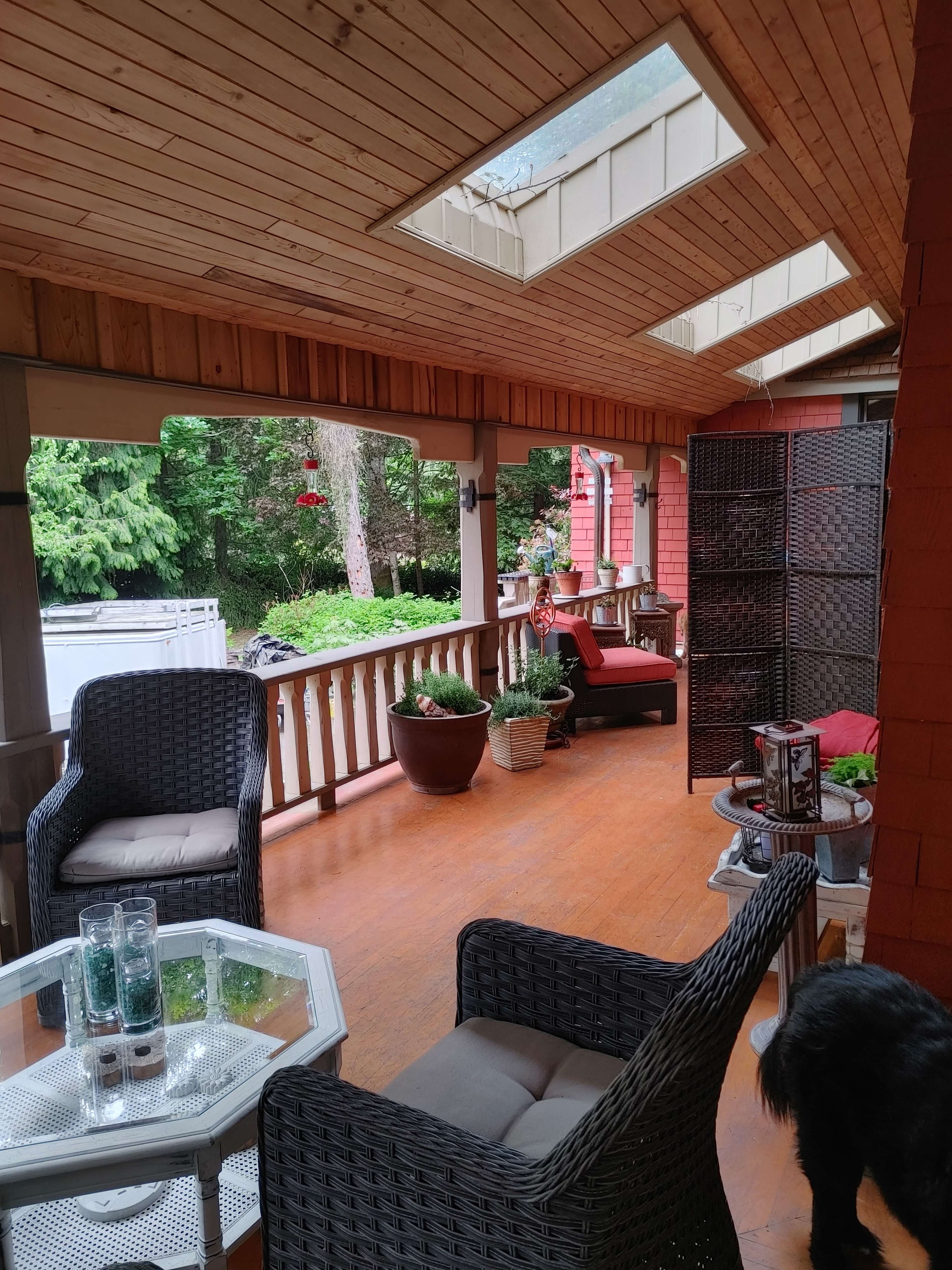 A covered porch with wicker chairs, a glass table, potted plants, and skylights above.
