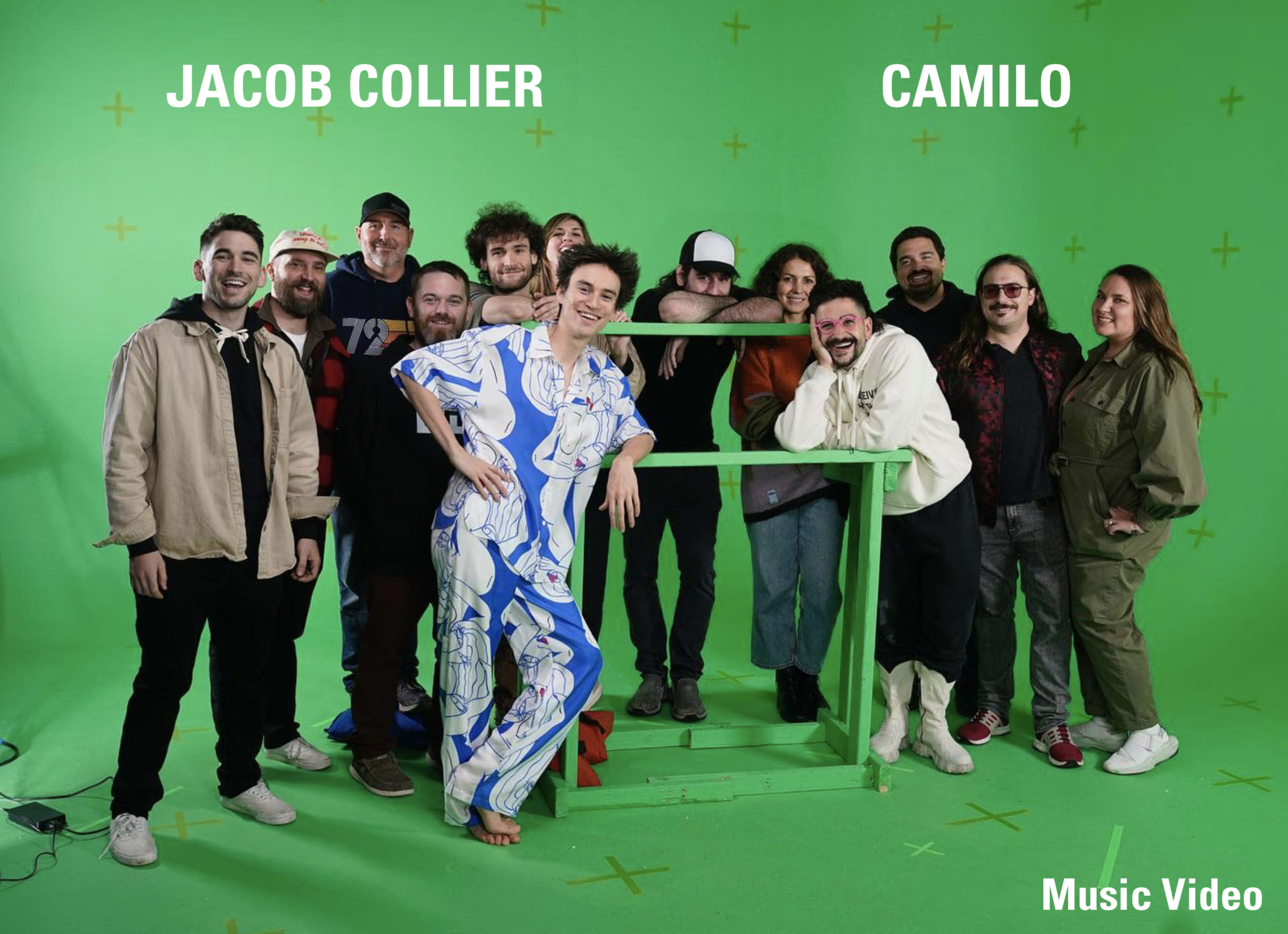 A group of people poses together in front of a green screen, with two individuals identified as Jacob Collier and Camilo.
