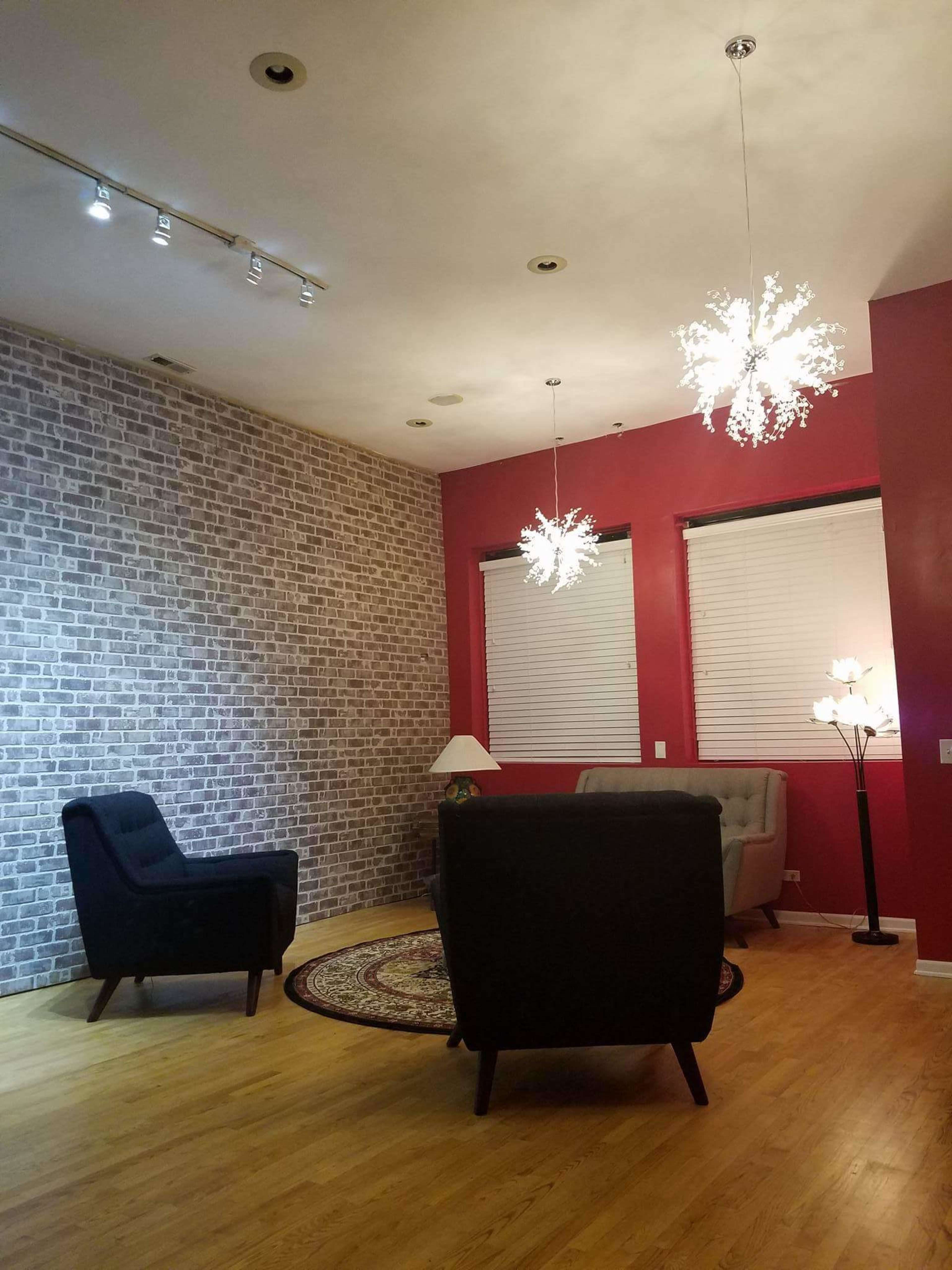 The room features a brick accent wall, two chairs, a rug, and modern light fixtures hanging from the ceiling.