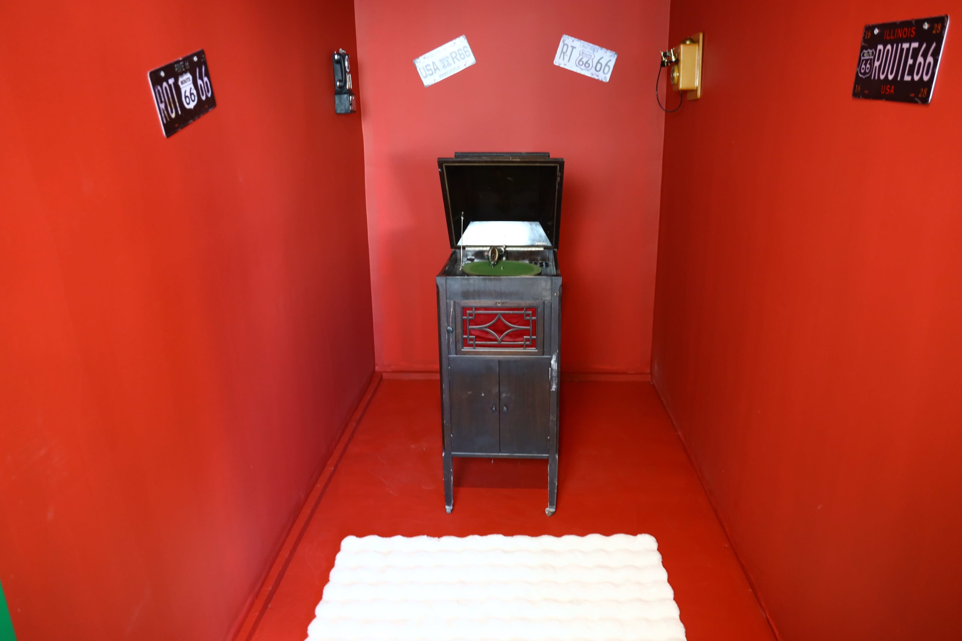 The scene shows a small, red-walled room featuring a vintage phonograph on a cabinet, with decorative Route 66 license plates on the walls.
