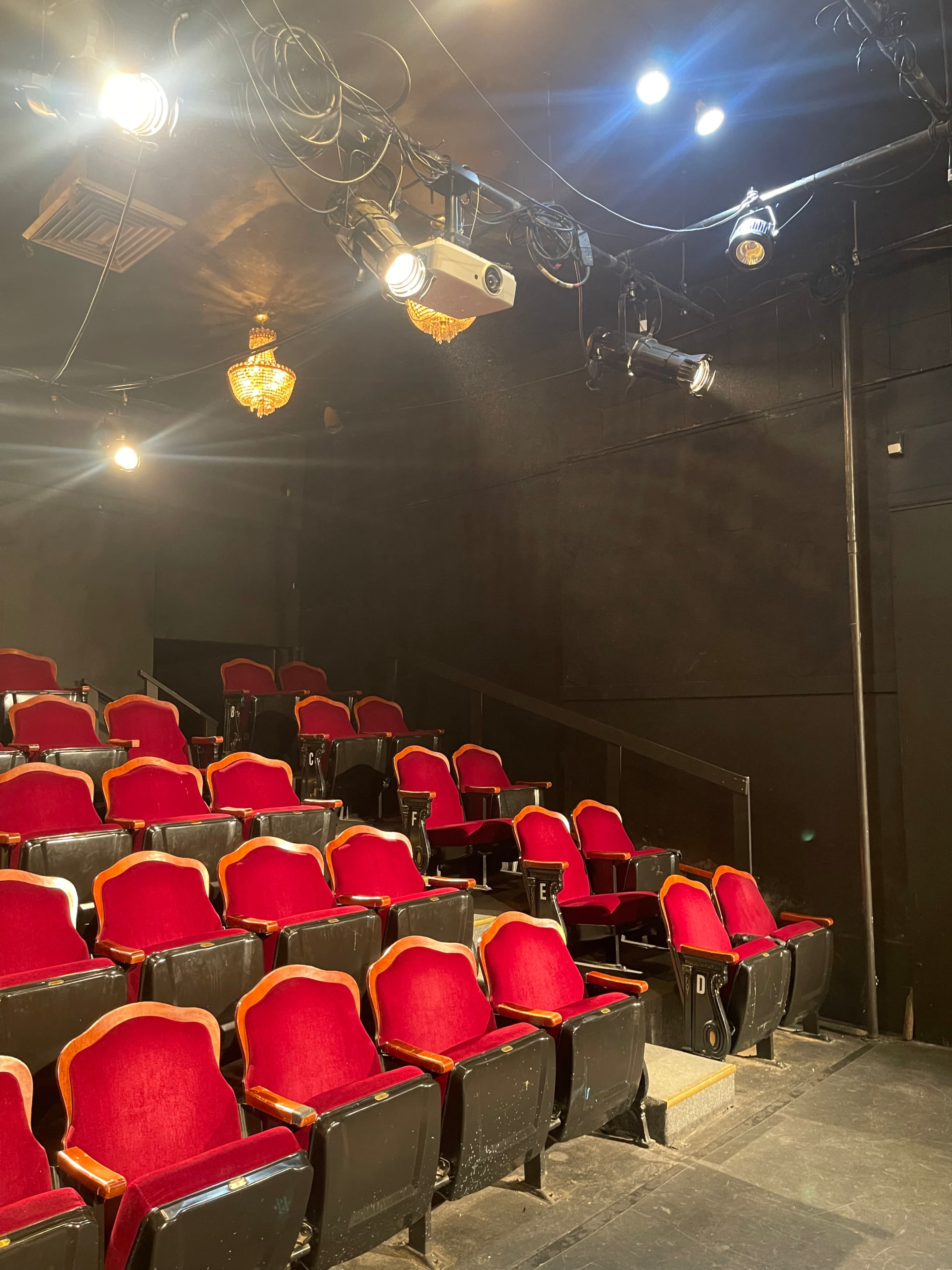 A theater interior with rows of red seats and overhead lighting fixtures.