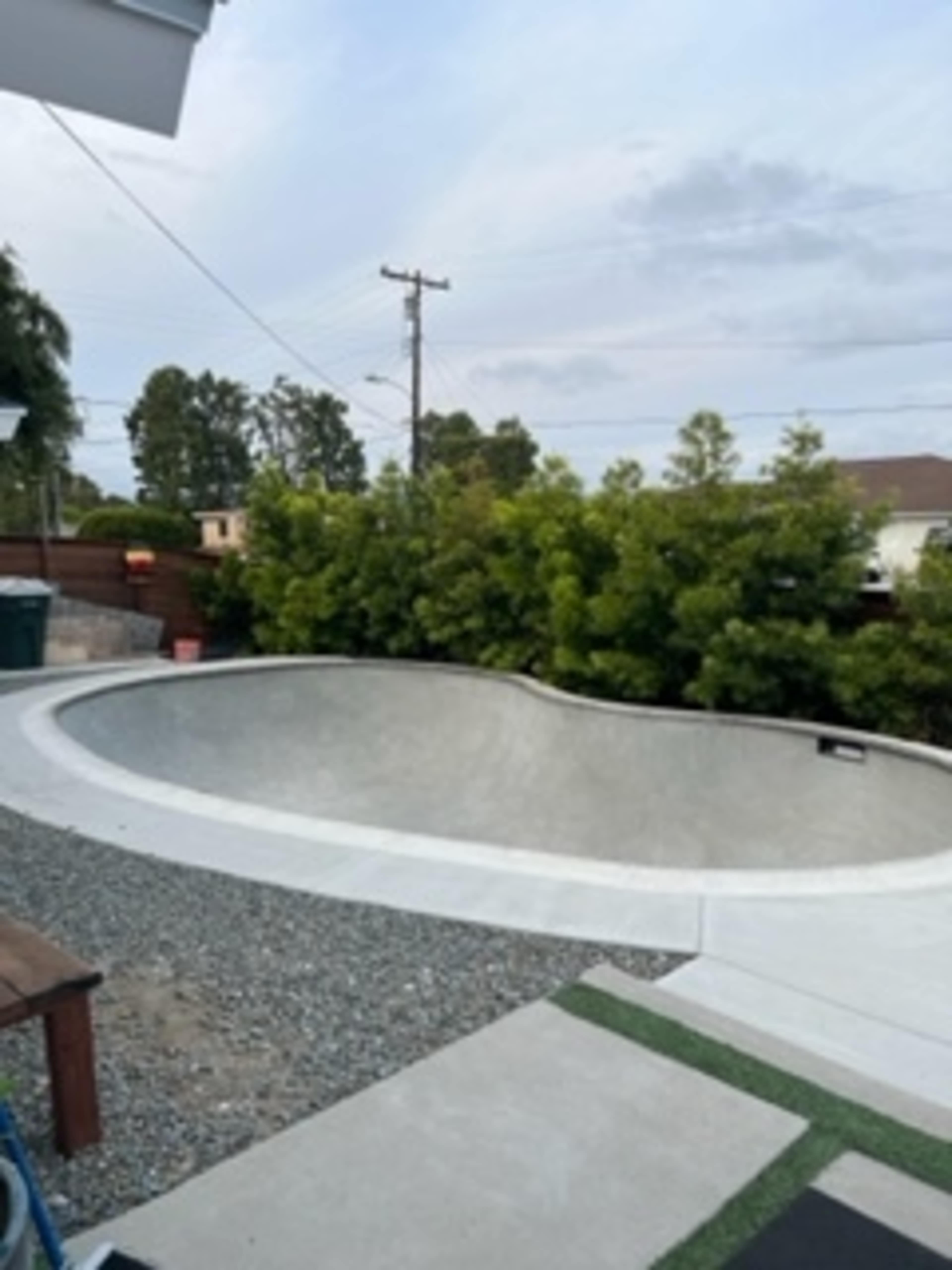 A concrete skate bowl surrounded by a landscaped area with shrubs and gravel.