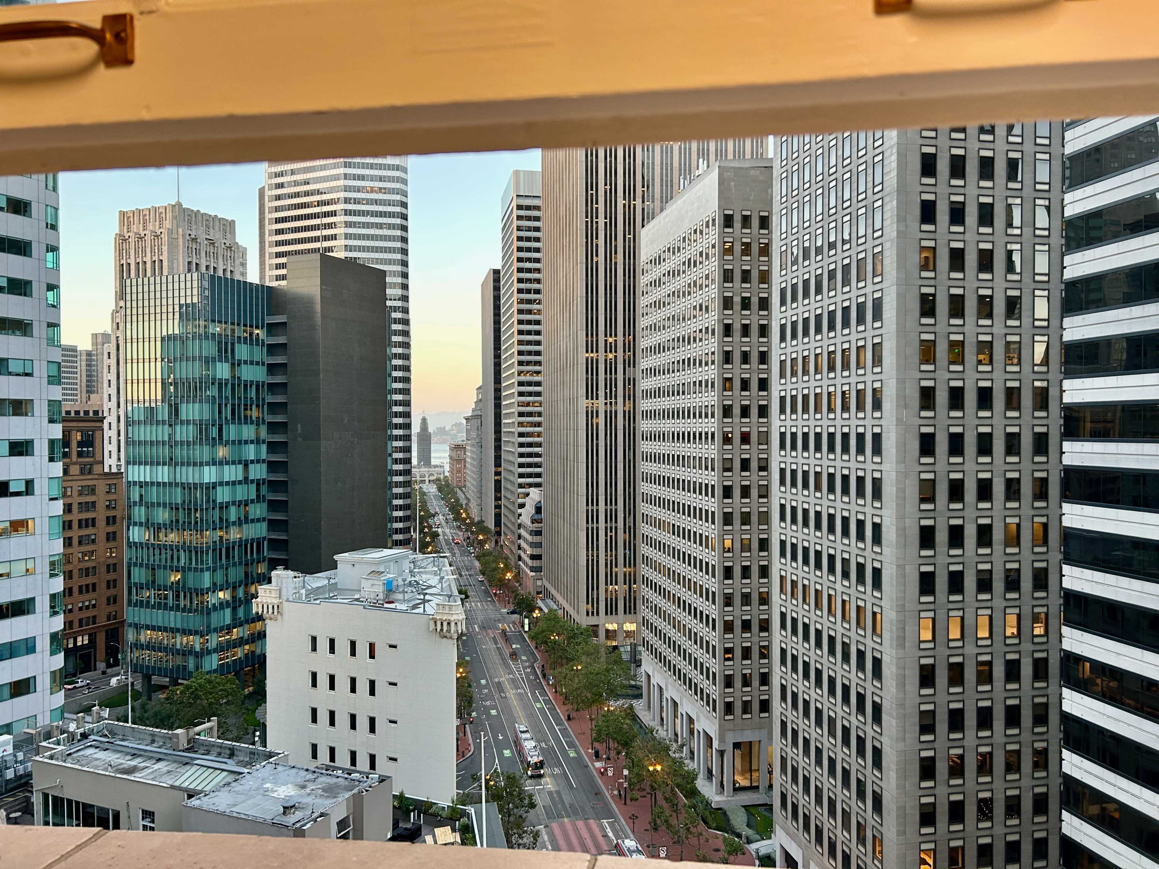 A view of a street lined with tall buildings in an urban setting, framed by a window.