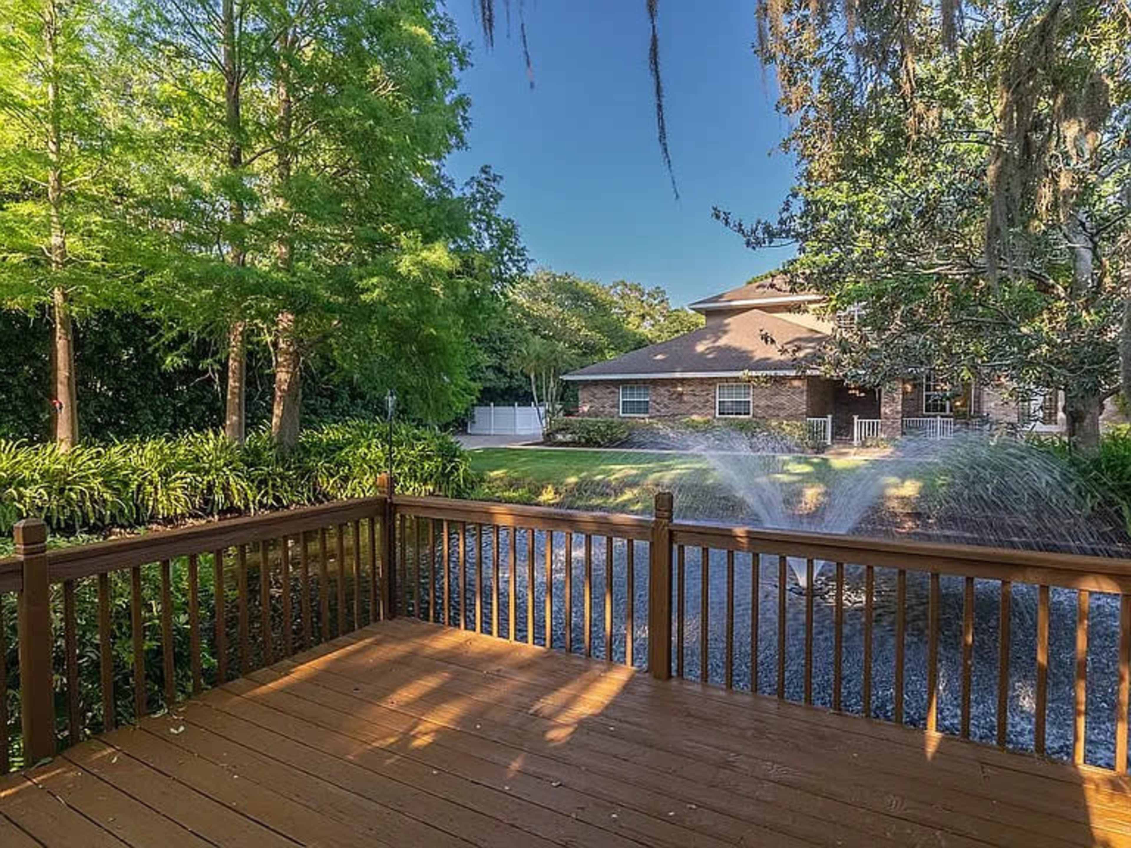 A wooden deck overlooks a landscaped yard with trees and a house in the background.