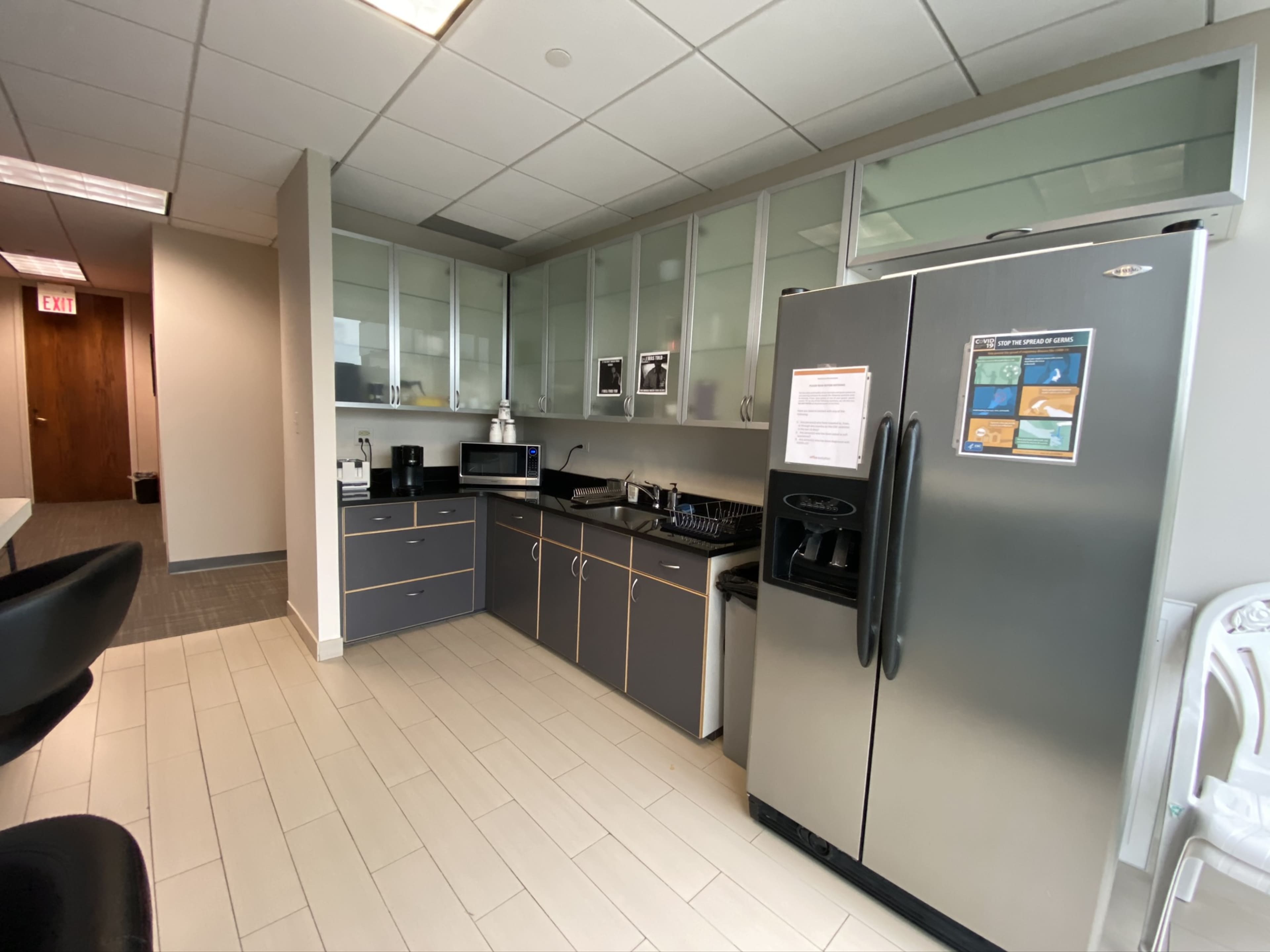 The image shows a modern kitchen area with gray cabinetry, a refrigerator, a microwave, and kitchenware neatly arranged on a countertop.