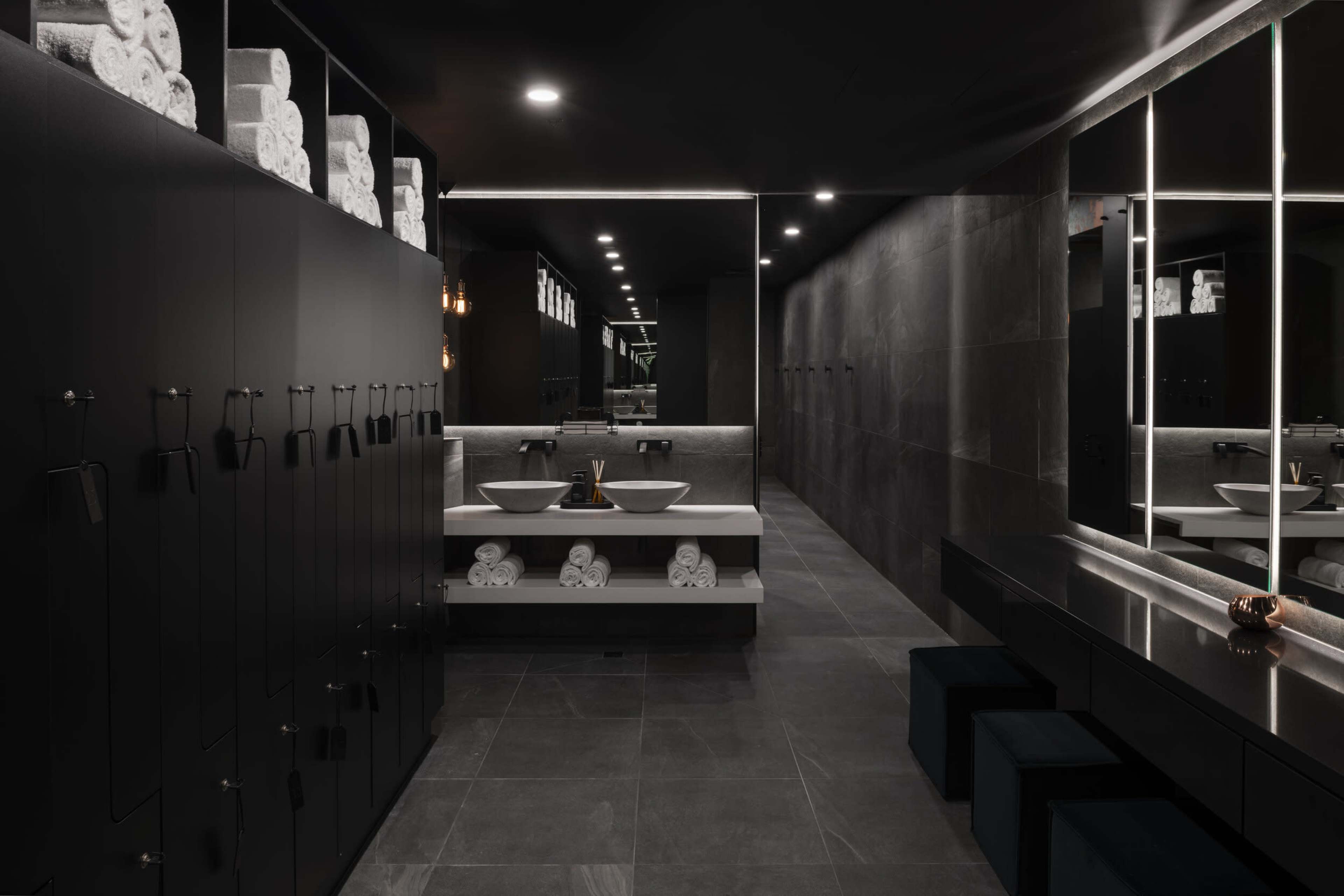 The image shows a modern bathroom with dark walls, dual sinks, and neatly arranged towels on shelves.