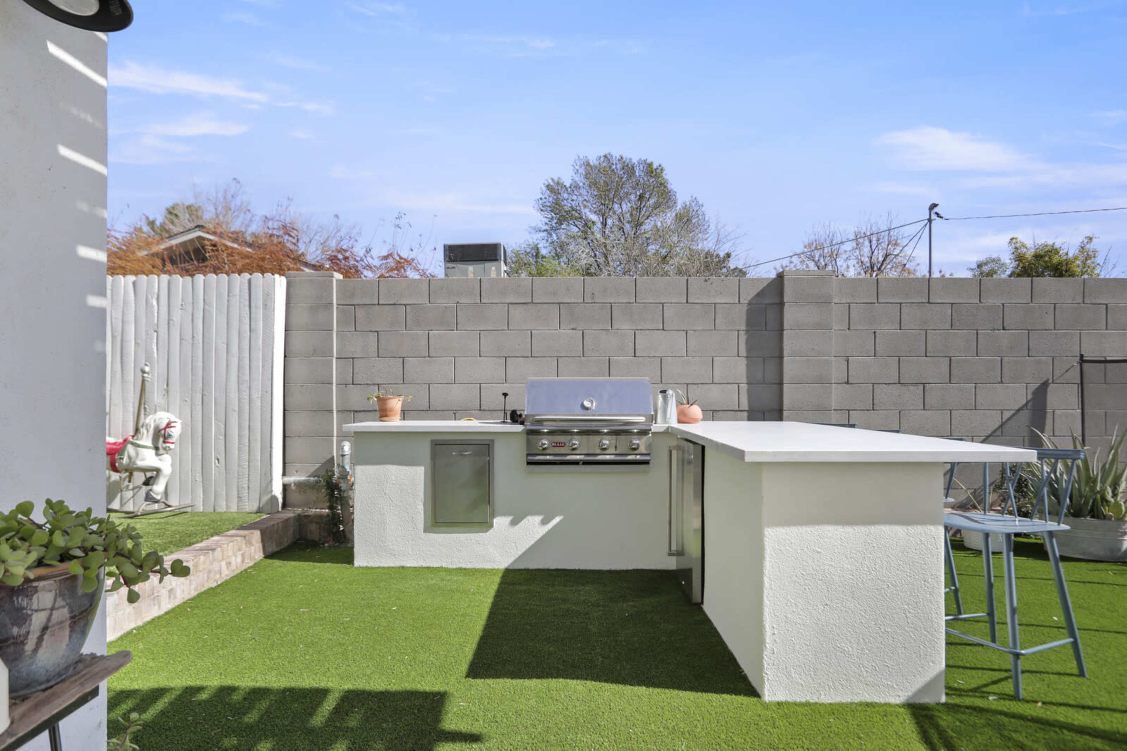 An outdoor kitchen area featuring a built-in grill, a countertop, and artificial grass in a fenced yard.