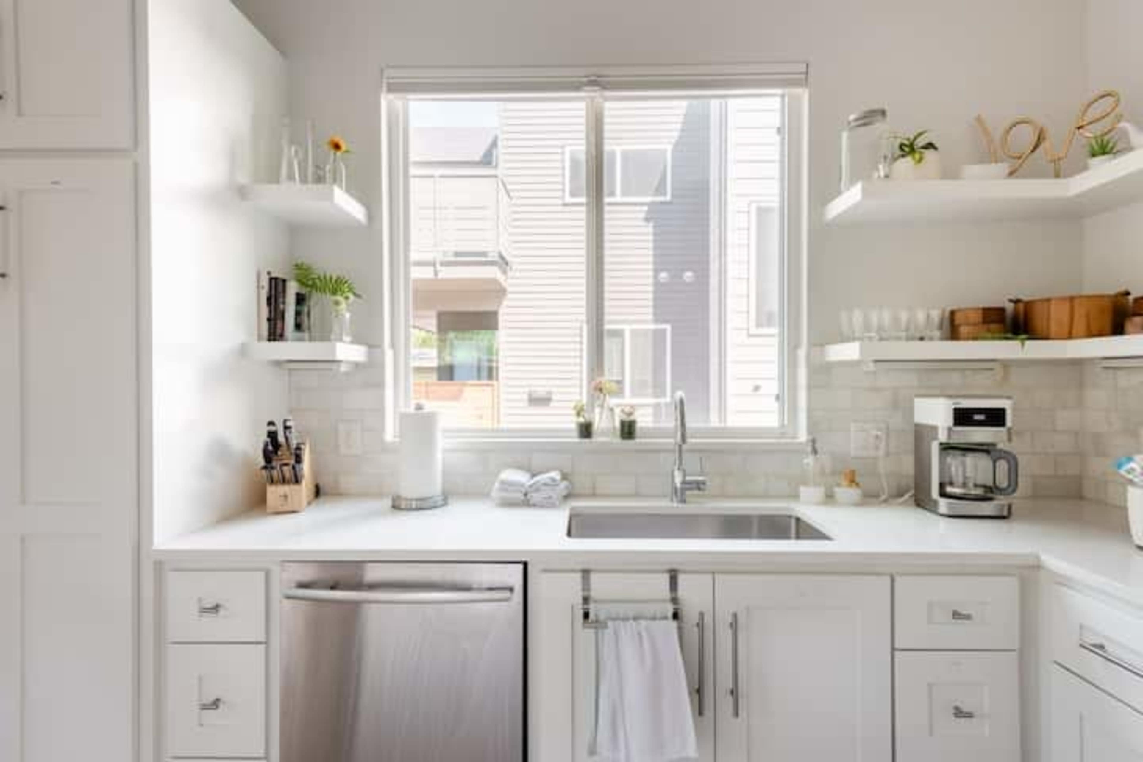 A modern kitchen with white cabinetry, a stainless steel sink, and a window overlooking an exterior view.