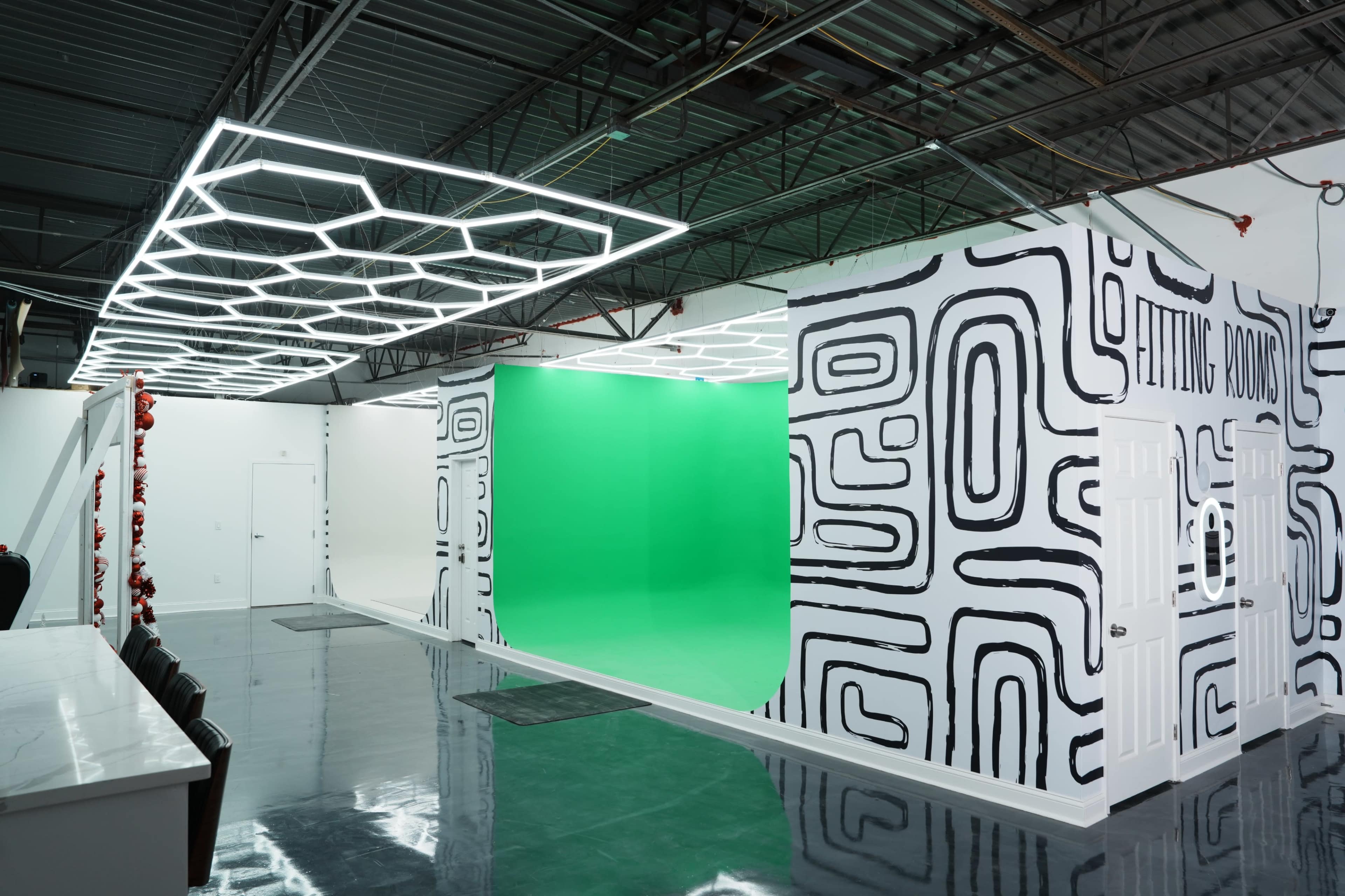 The image shows a modern studio space featuring a green screen area, geometric-patterned walls, and bright overhead lighting.