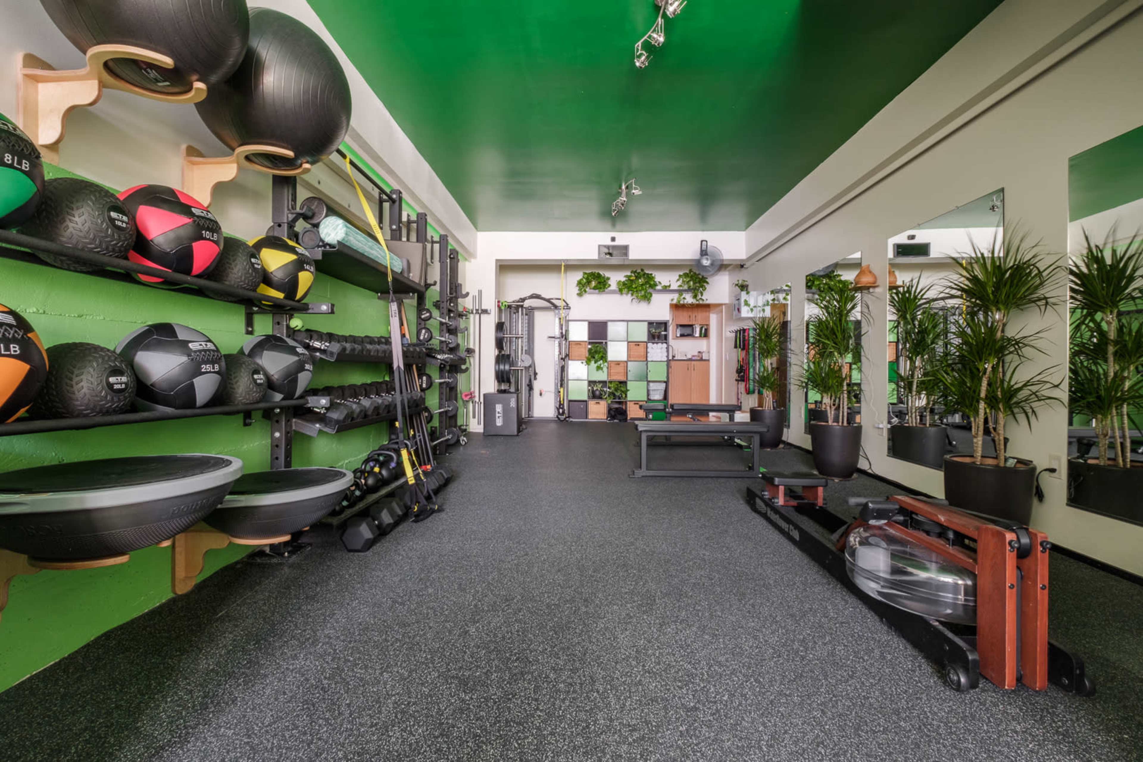 The image shows a well-equipped fitness studio with various exercise equipment, including weights and resistance bands, set against a green and black color scheme.