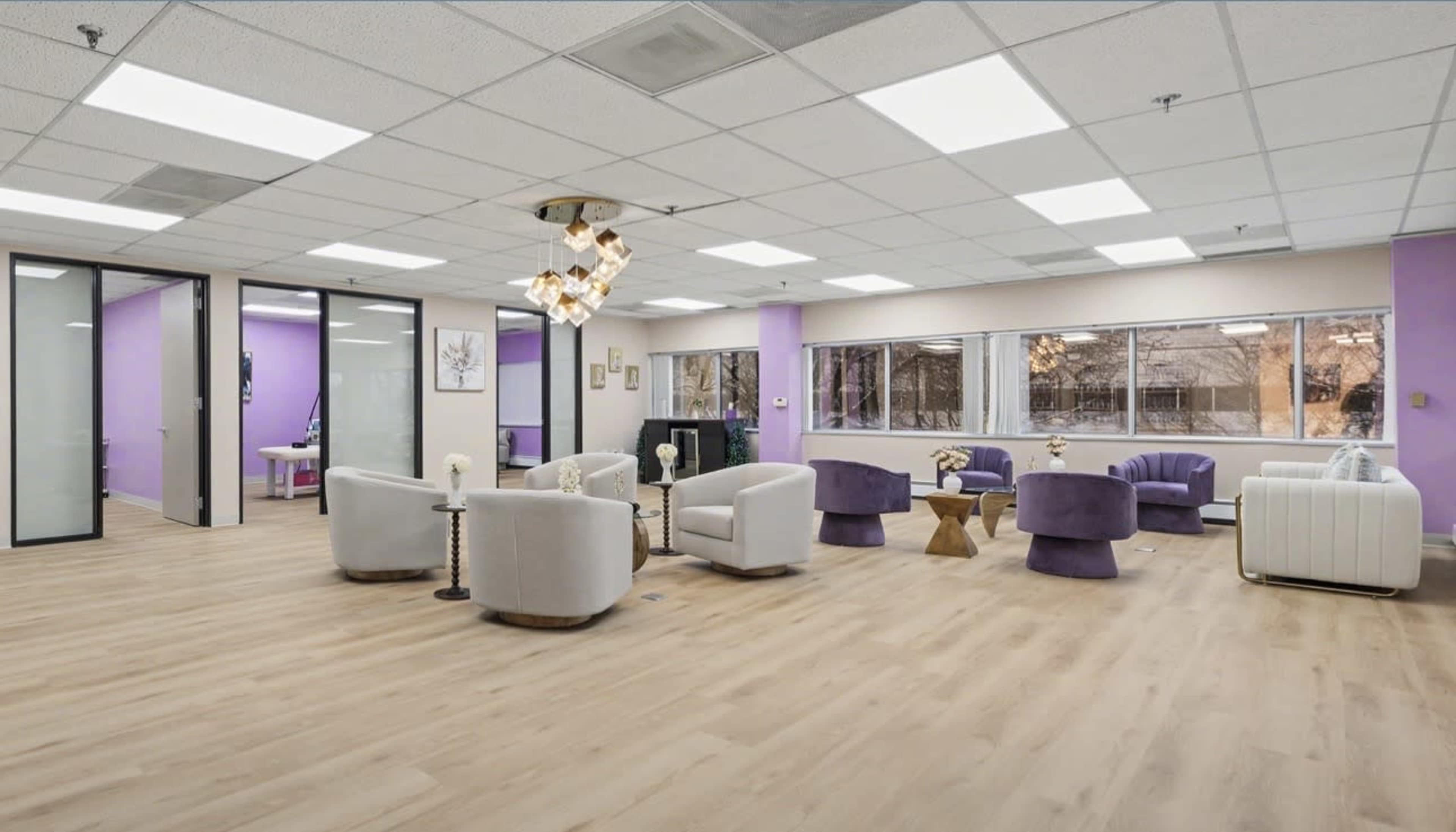 The image shows a modern office space with light wood flooring, purple accent walls, and contemporary seating arrangements.