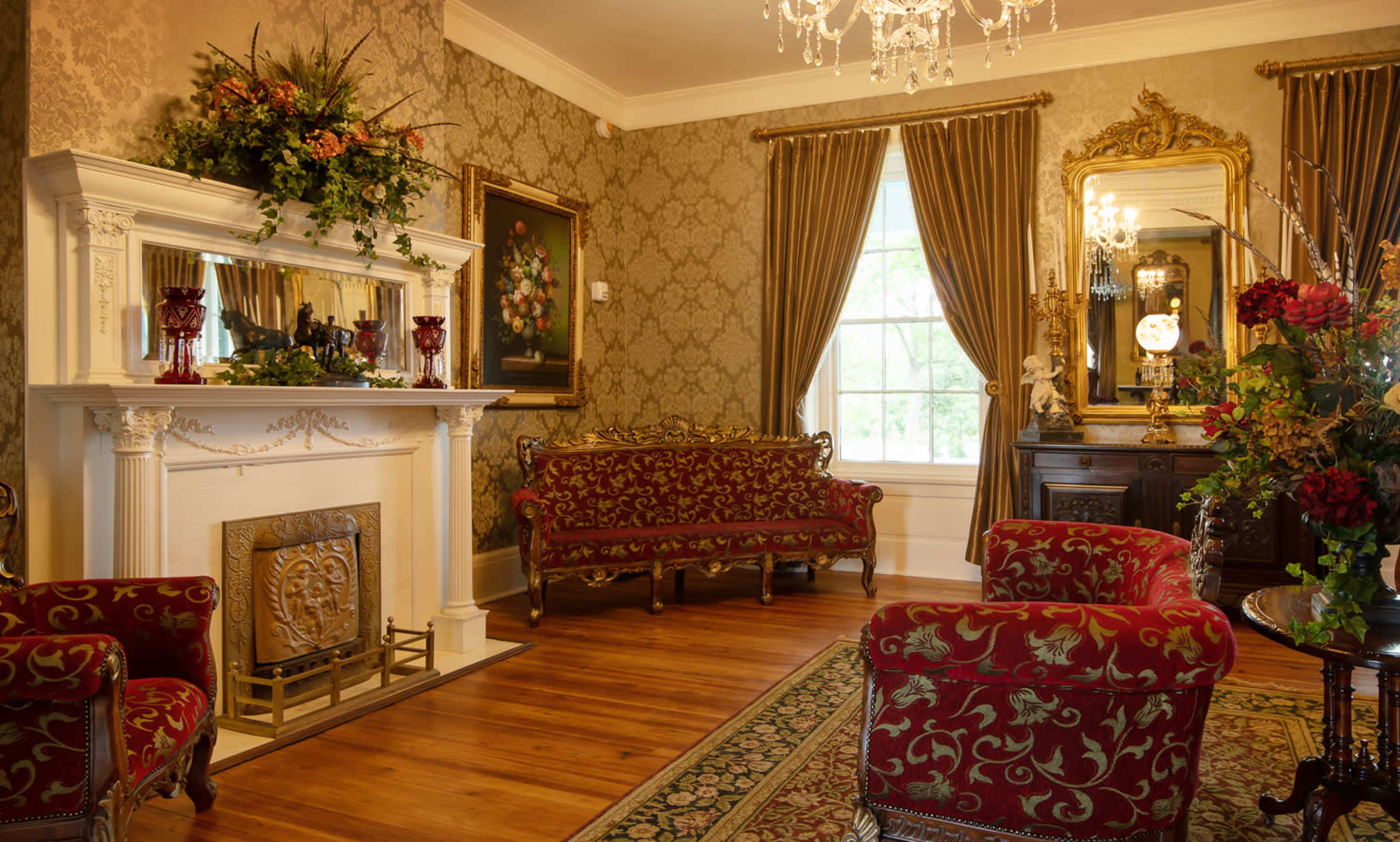 The room features a decorative fireplace, ornate furniture, and rich floral accents, creating an elegant atmosphere.