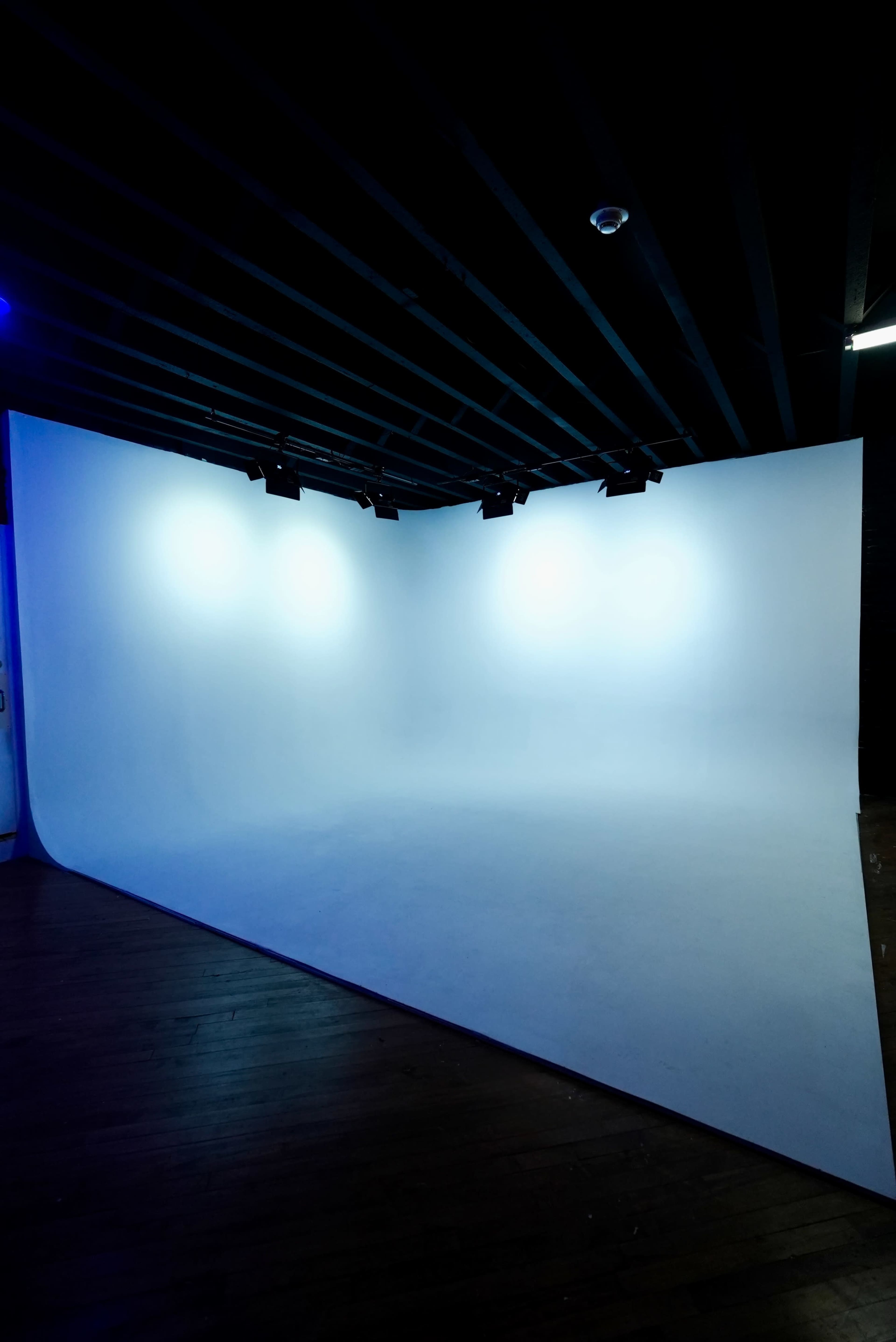 The image shows a photography studio with a large, curved white backdrop and dim lighting from above.