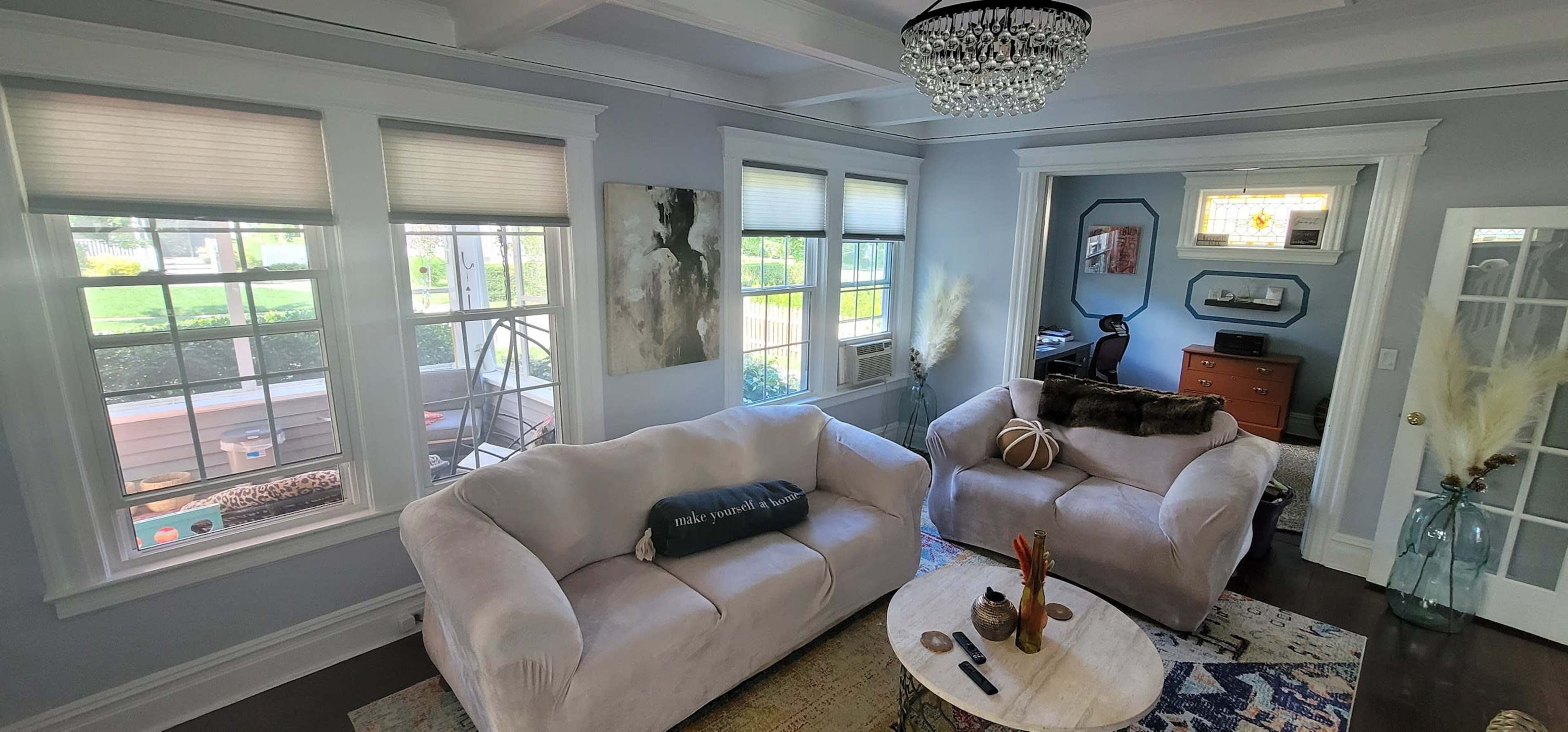 A bright living room features two light-colored sofas, a round coffee table, and large windows that let in natural light.