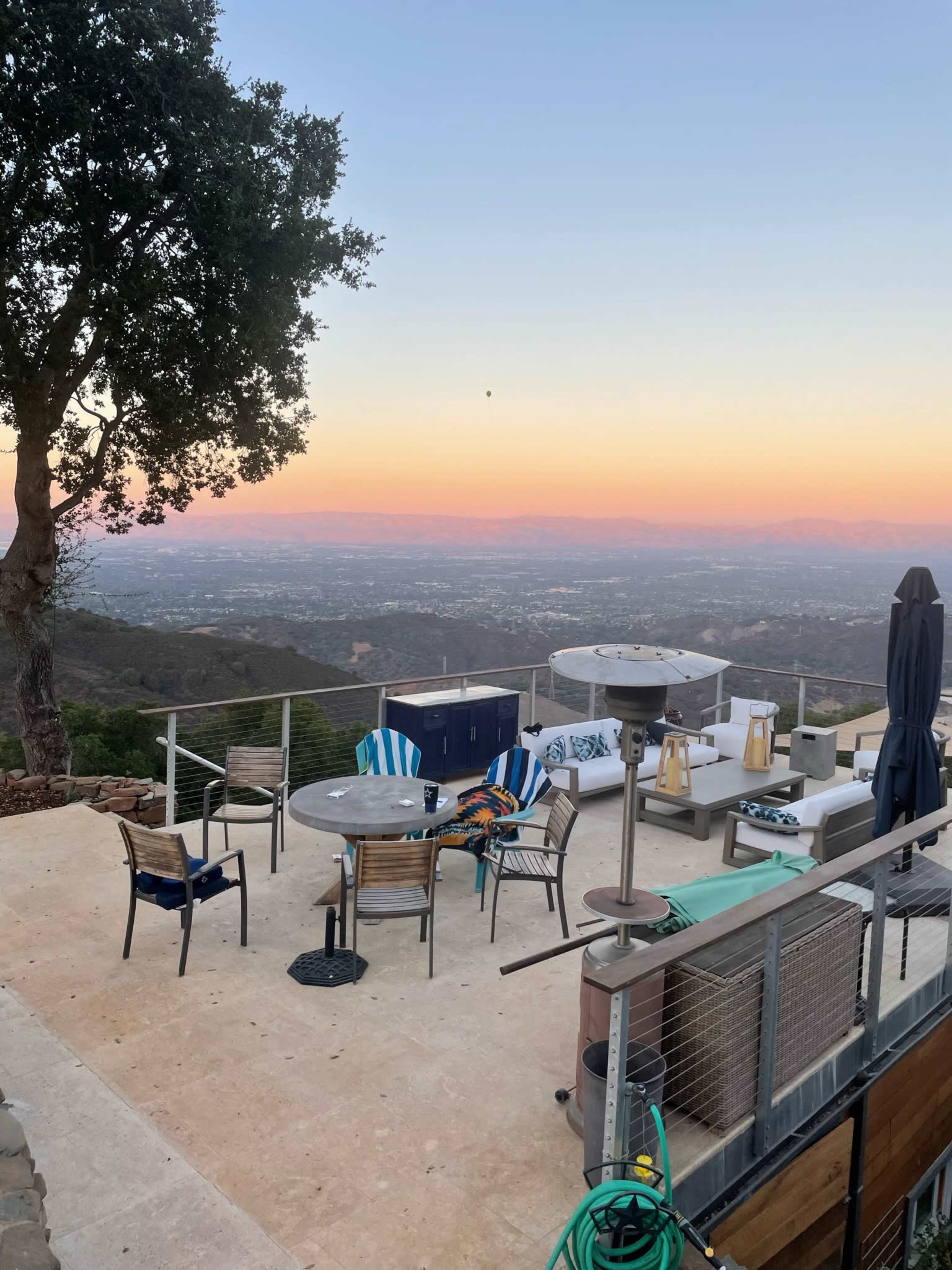 A spacious outdoor patio area with seating and tables, overlooking a valley during sunset.
