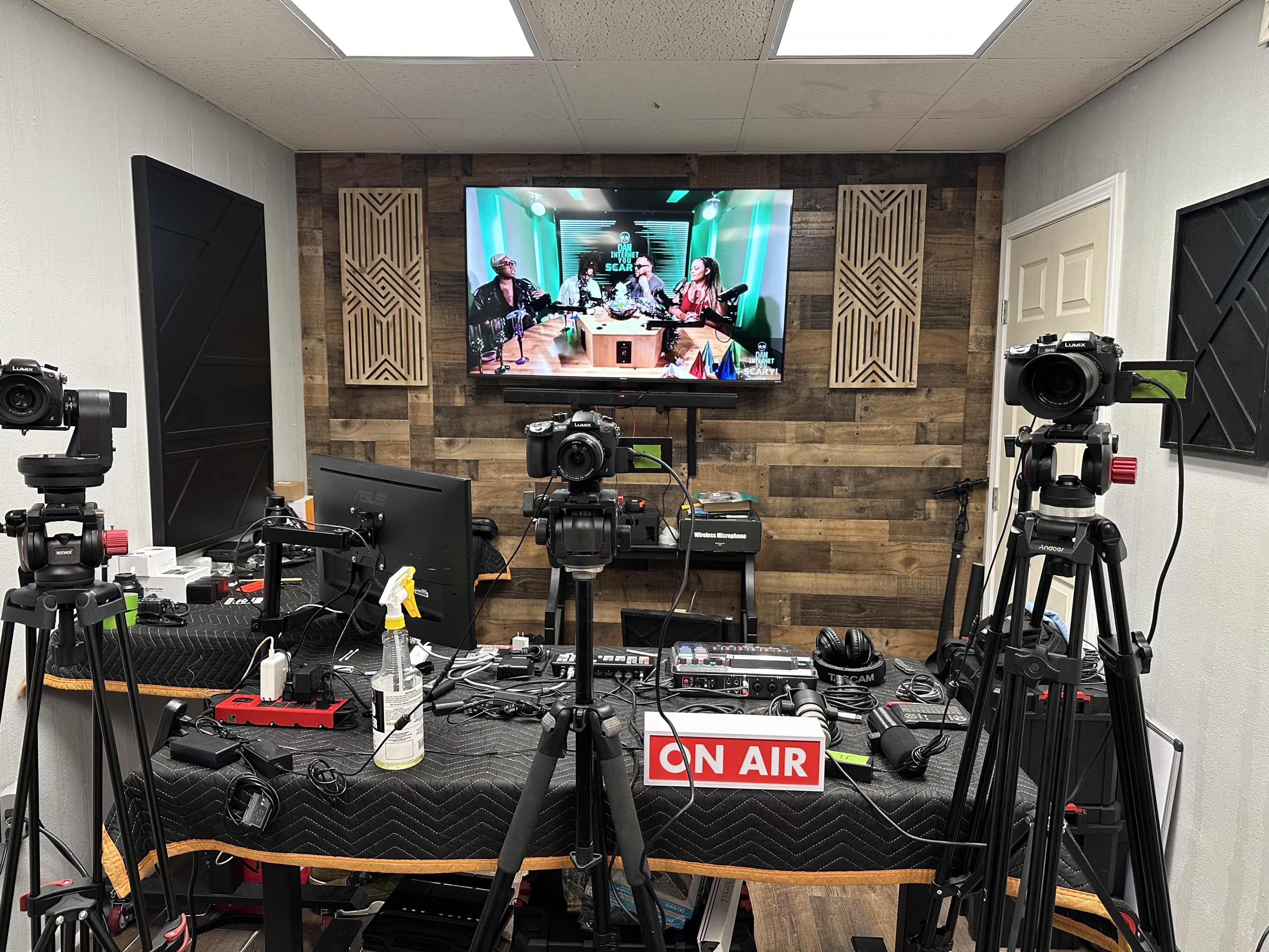 The image shows a recording studio equipped with multiple cameras, a soundboard, and a large screen displaying a video podcast featuring three individuals.