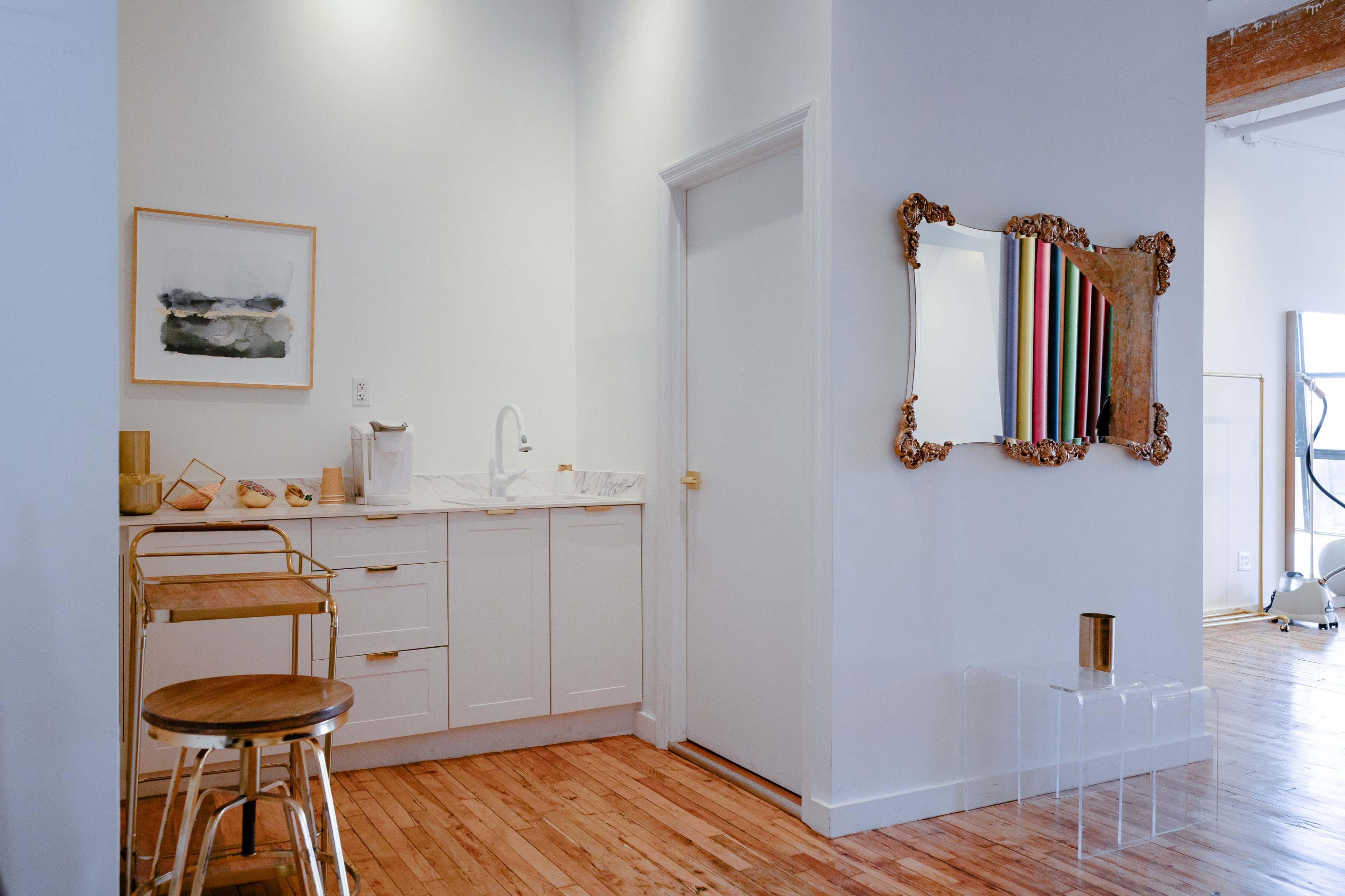 A well-lit corner of a modern kitchen featuring white cabinetry, a small cart, and a decorative mirror on the wall.