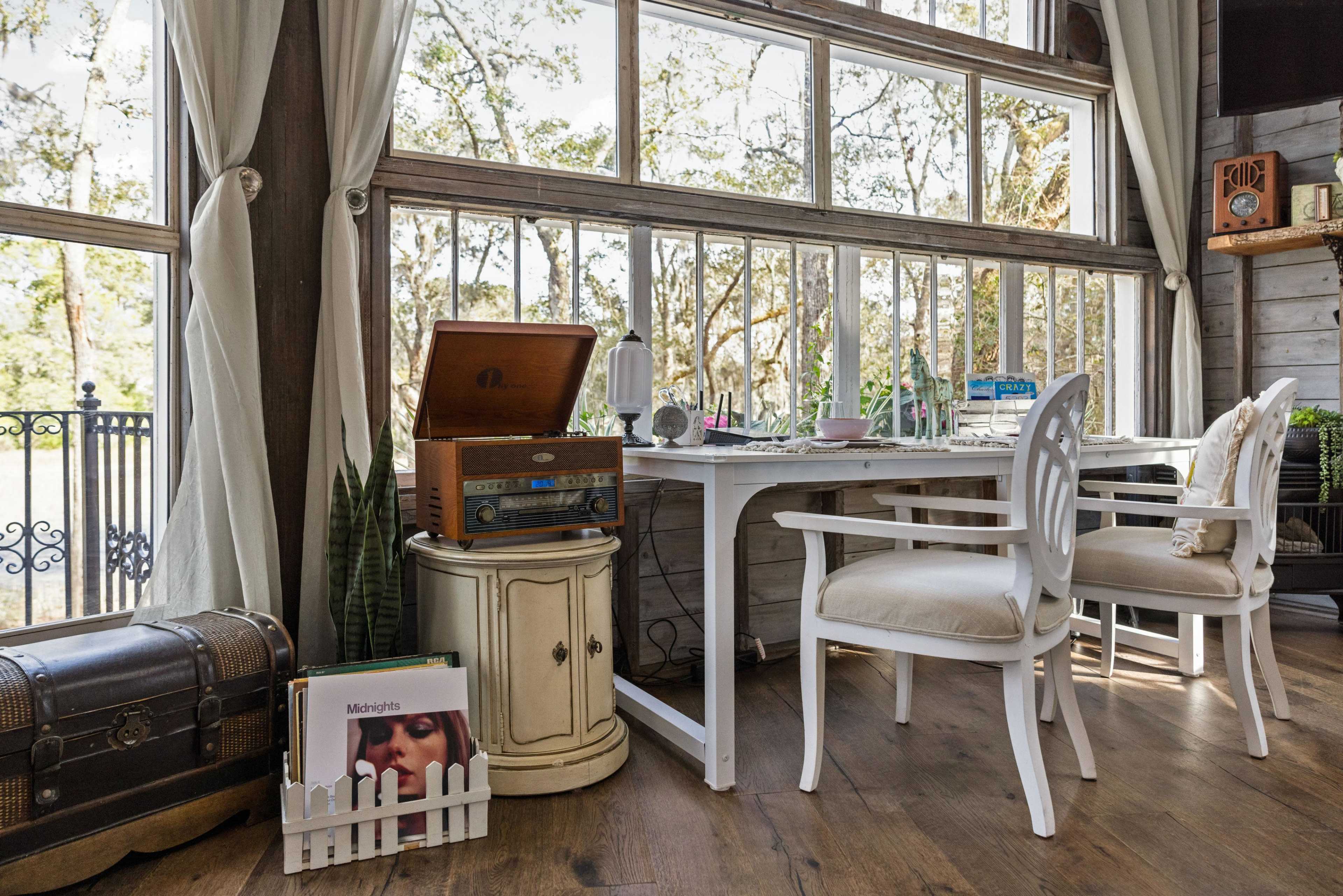 A cozy indoor workspace with a vintage record player, a small table, and a window overlooking a tree-filled landscape.