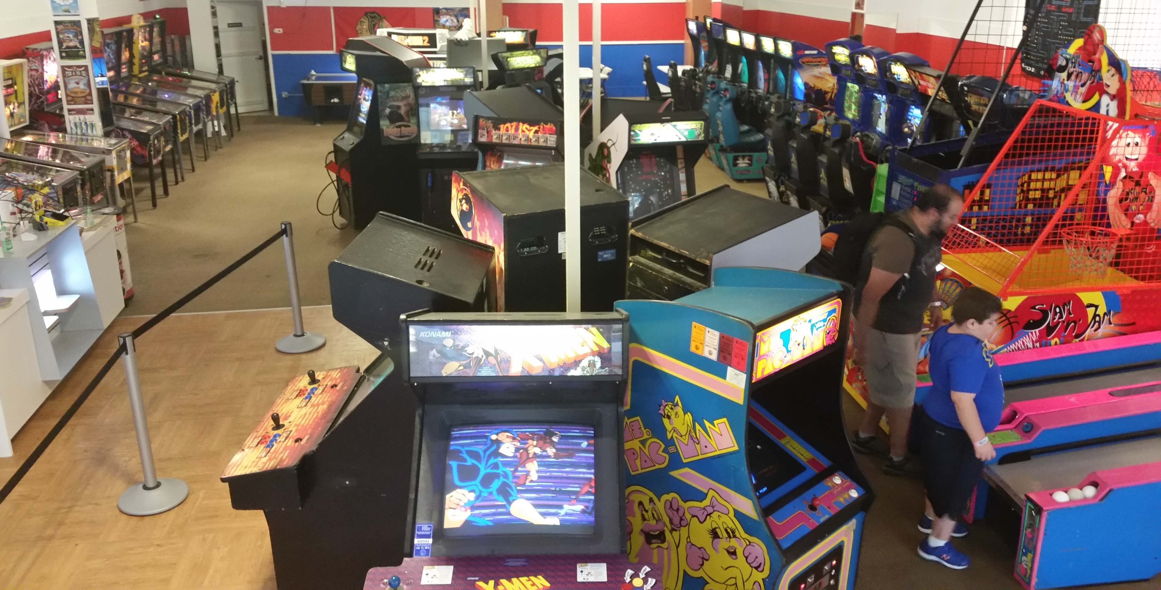 The image shows an arcade featuring a variety of pinball machines and classic video game cabinets arranged in a spacious room.