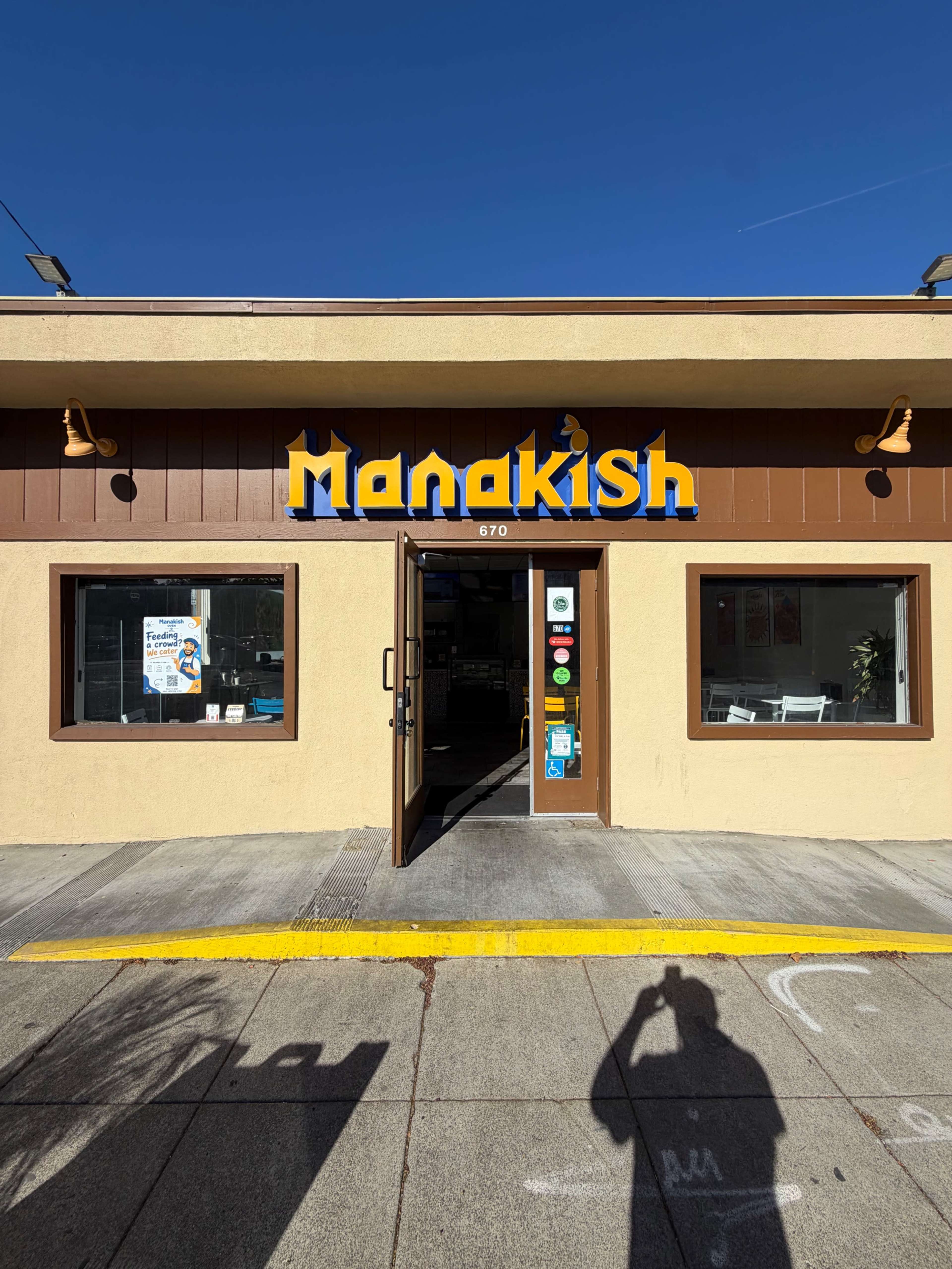 The image shows the entrance of a business named "Manakish," with a brightly colored sign and a clear view of the interior beyond the open door.