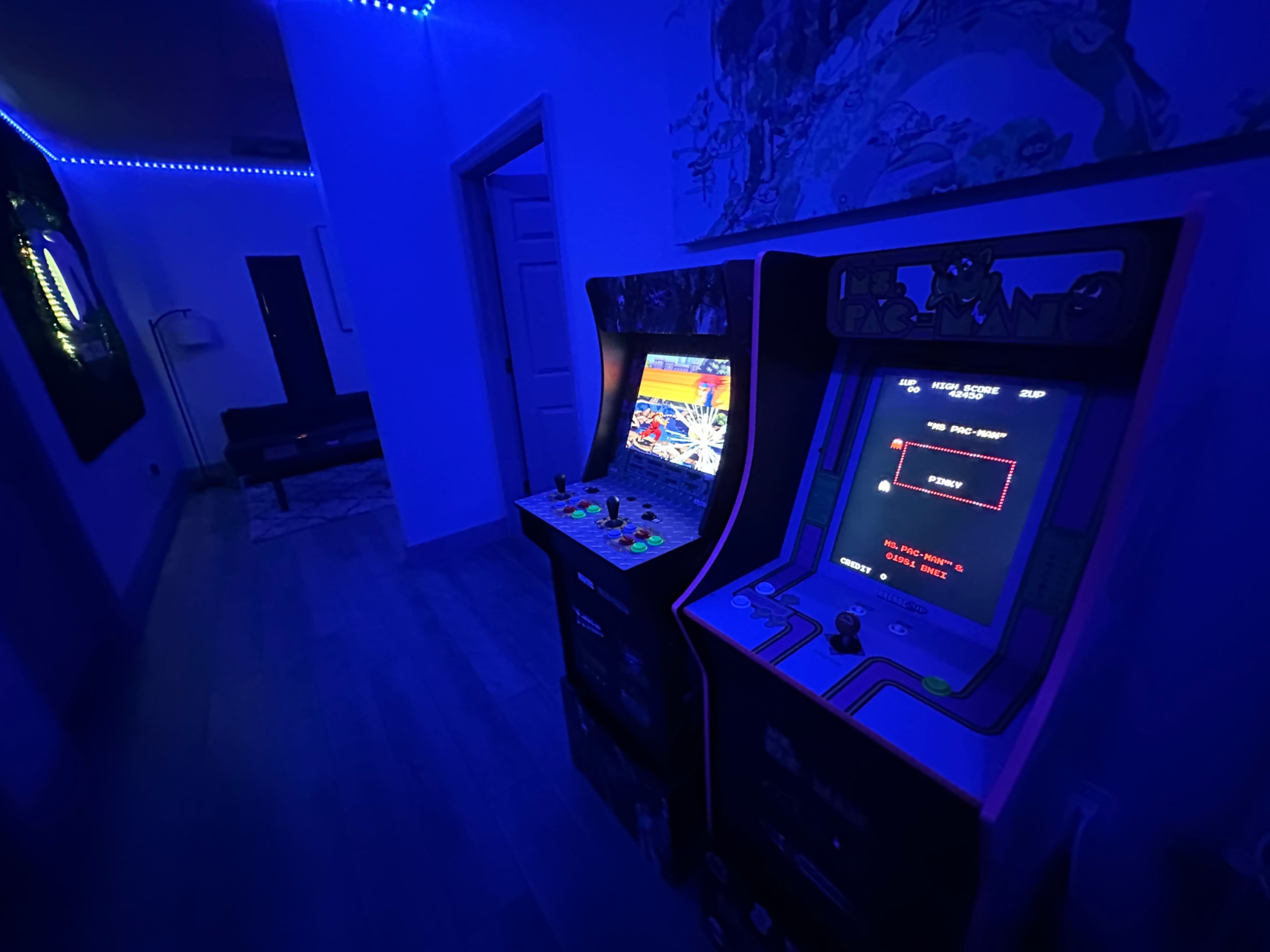 Two arcade game machines illuminated by blue LED lights in a dimly lit hallway.