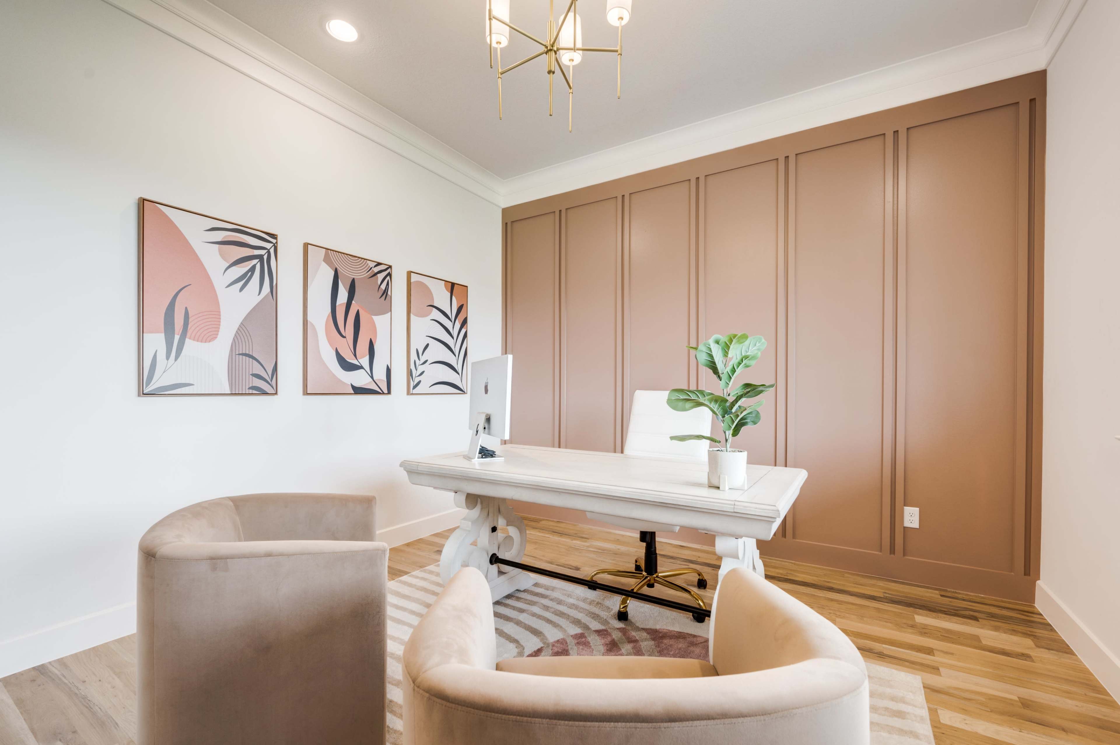 A modern office features a white desk with an iMac, two beige chairs, and wall art, all set against a warm brown panelled wall.