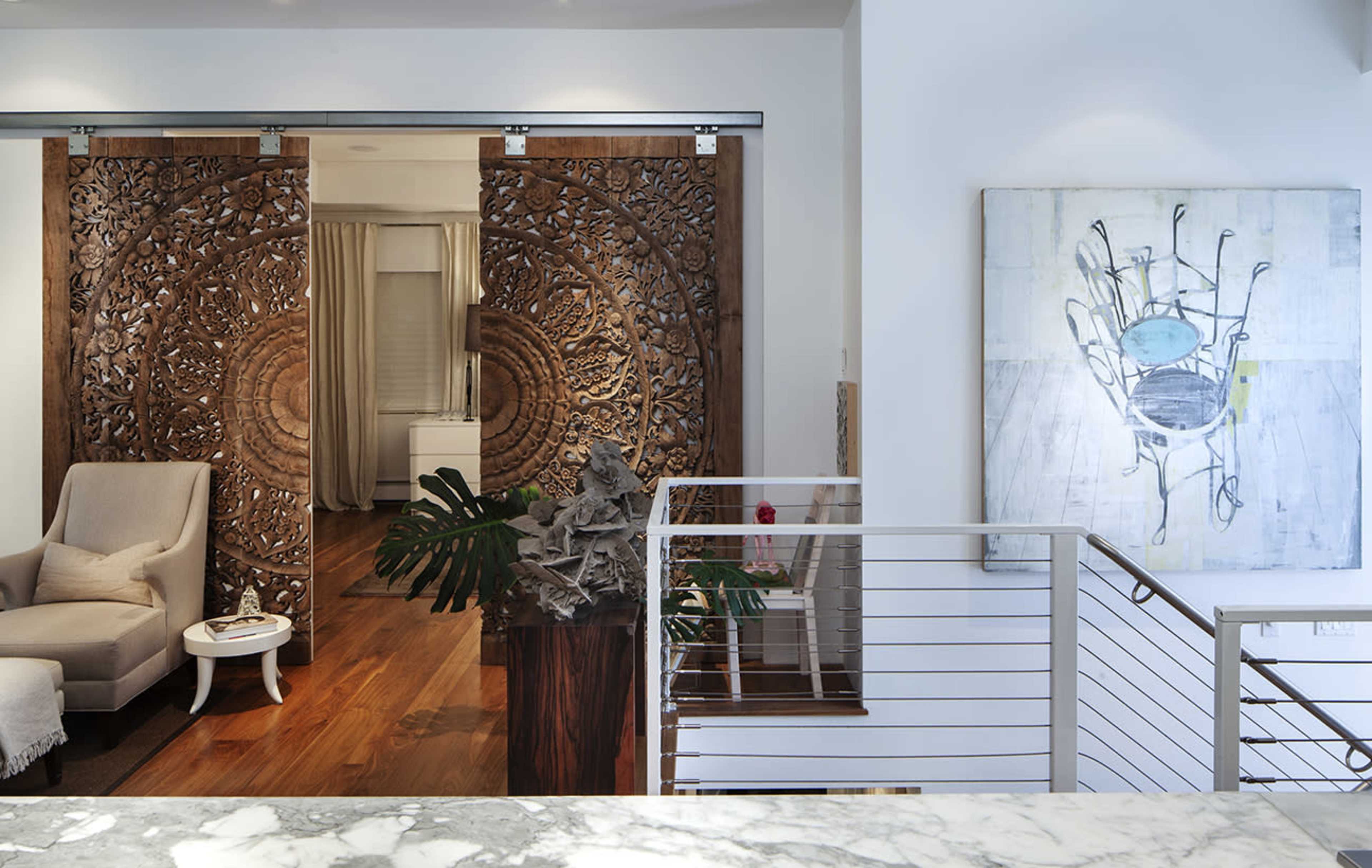 The image shows a modern interior featuring a seating area with an upholstered armchair, decorative wooden sliding doors, and a large abstract painting on the wall.